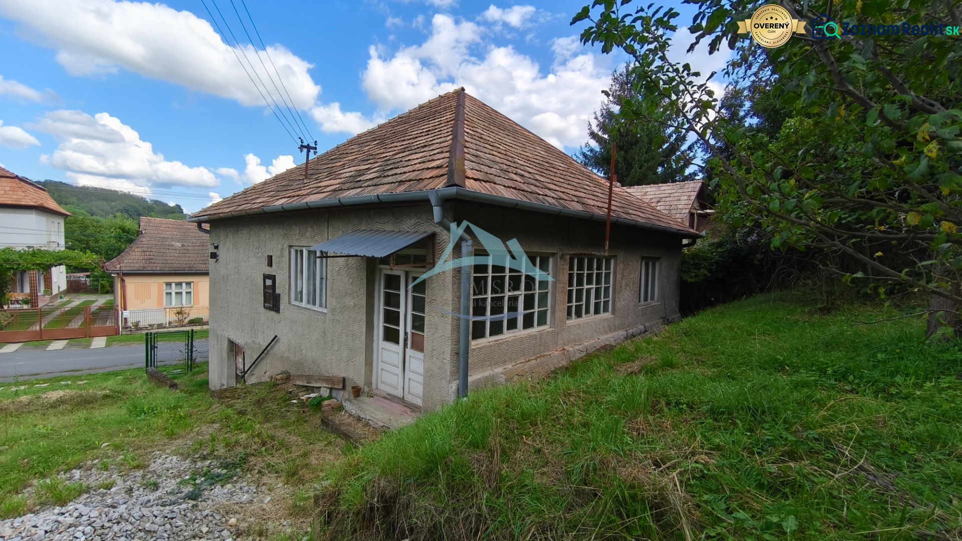 A family house in Olováry with a sloped roof, surrounded by a garden and green trees.
