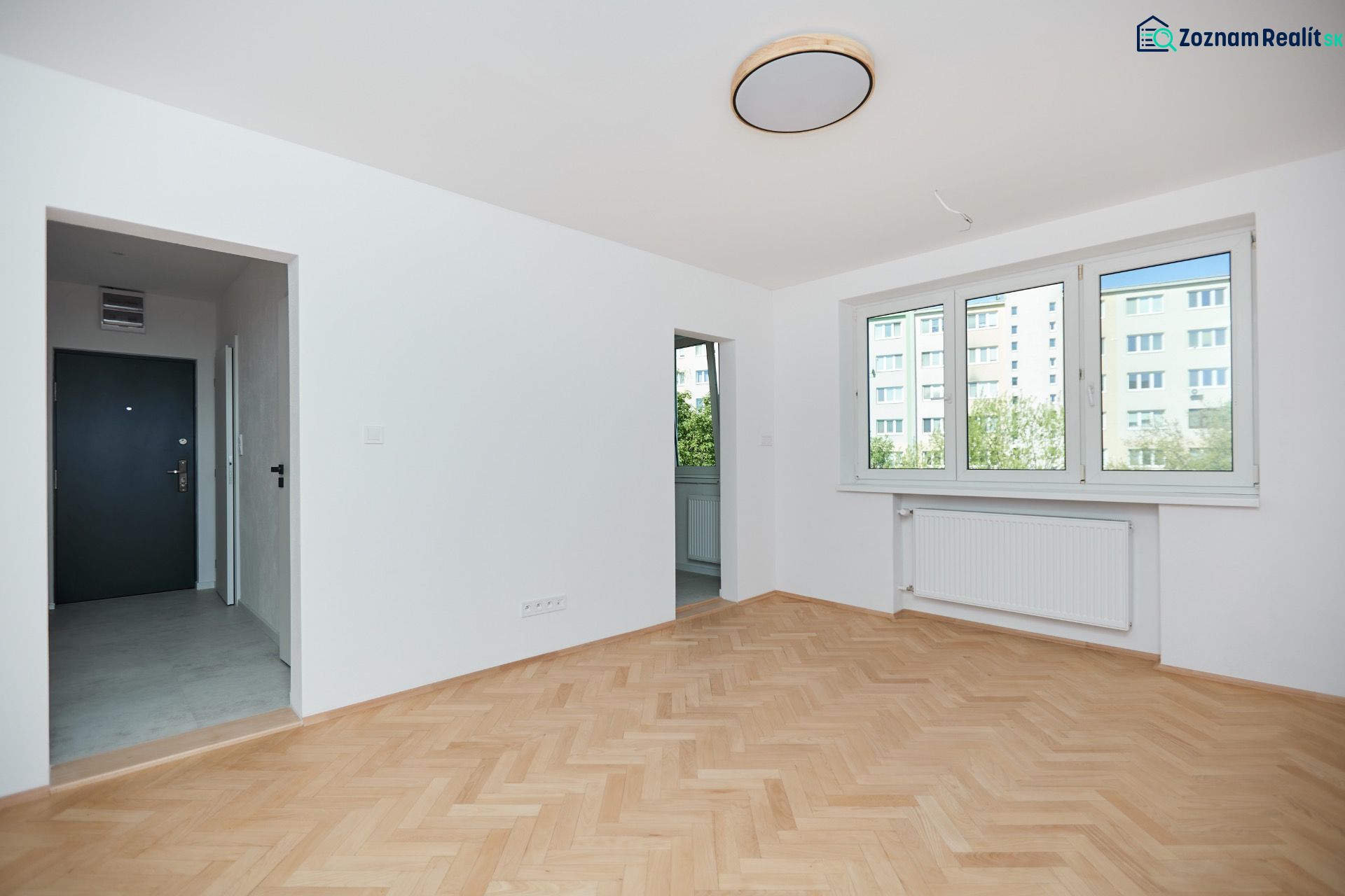 An apartment with a wooden floor design, white walls, and large windows.