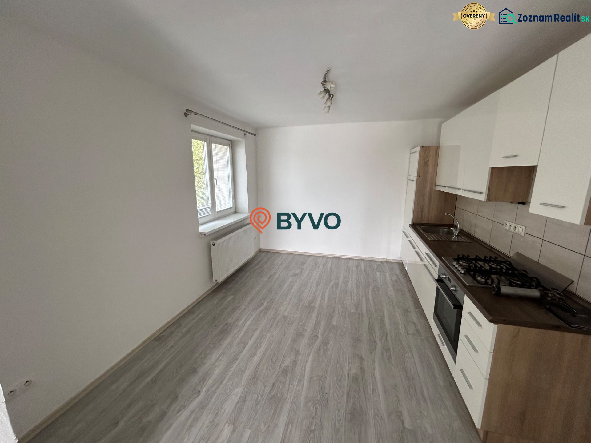 A kitchen with a white unit in a 3-room apartment, a floor with a wooden decor, a large window.