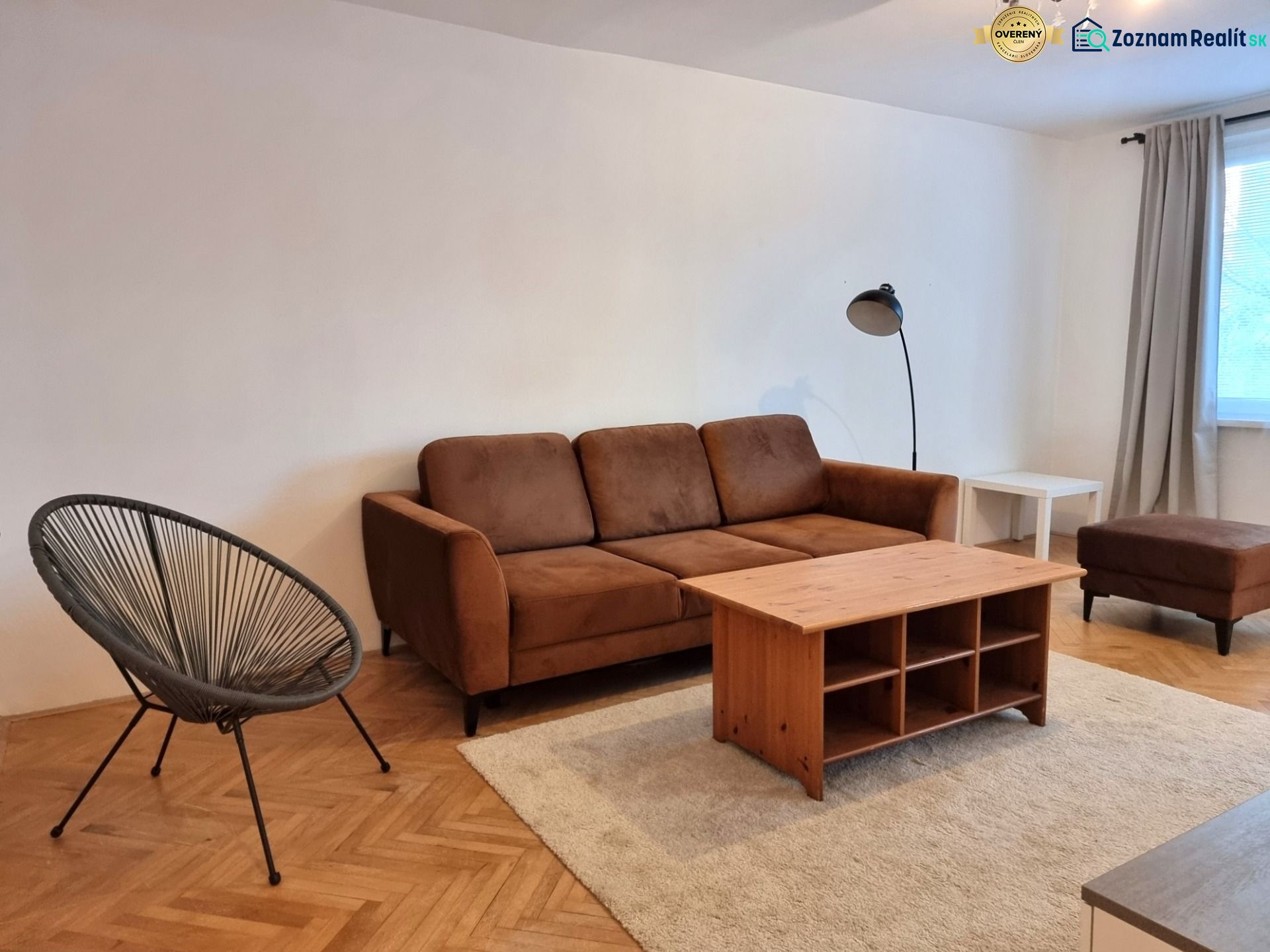 Living room of a two-room apartment with a brown sofa and a floor with a wooden decor.