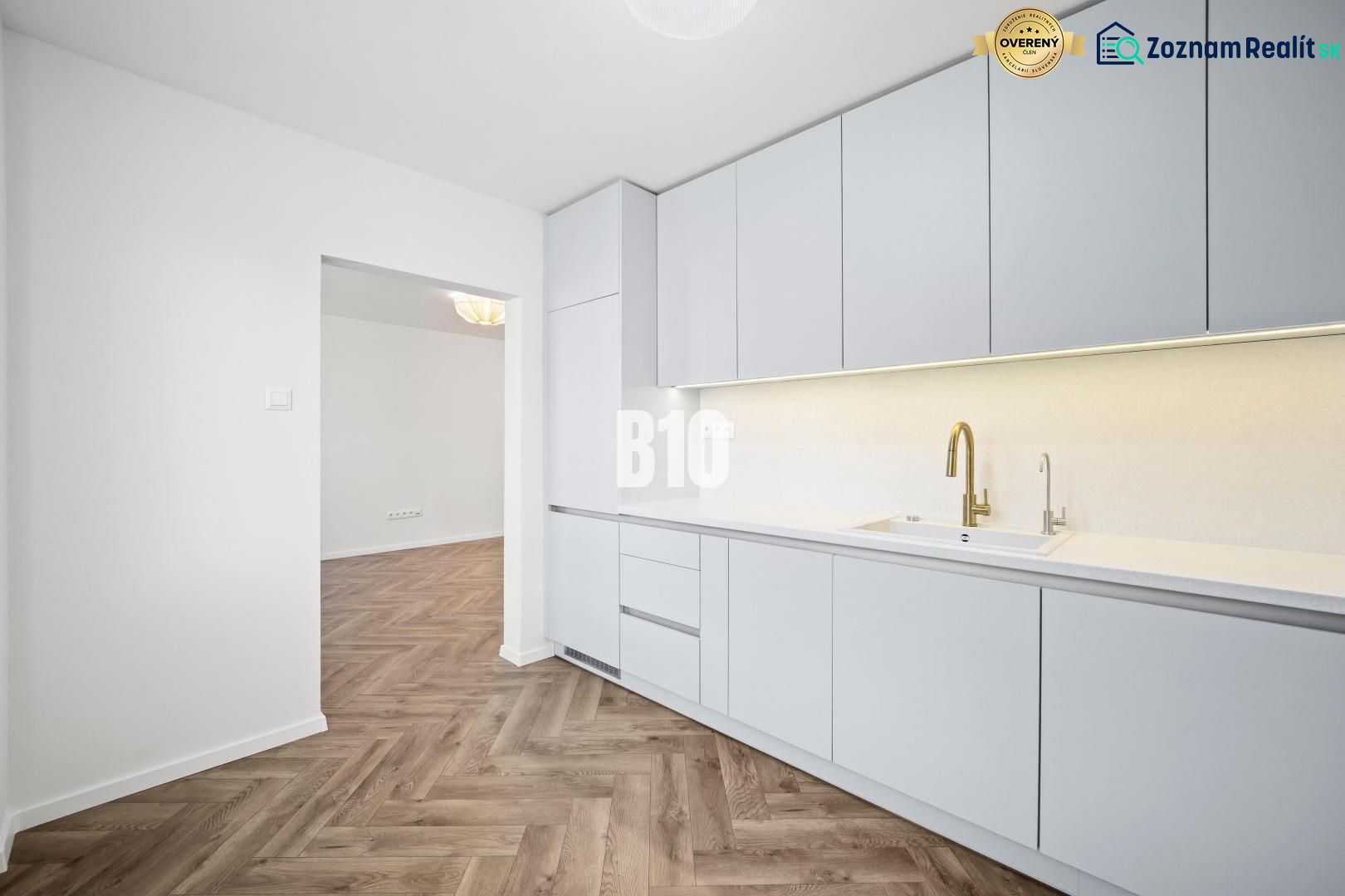 A kitchen in a 3-room apartment with white furniture and a wooden decor floor.