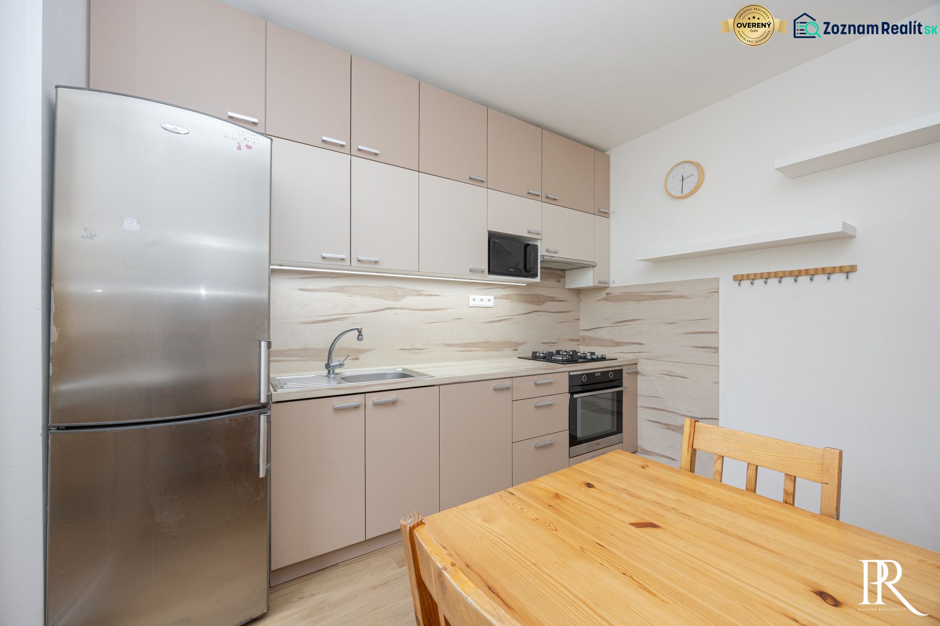 A kitchen in a 3-room apartment with a refrigerator, a wooden table, and a kitchen unit.