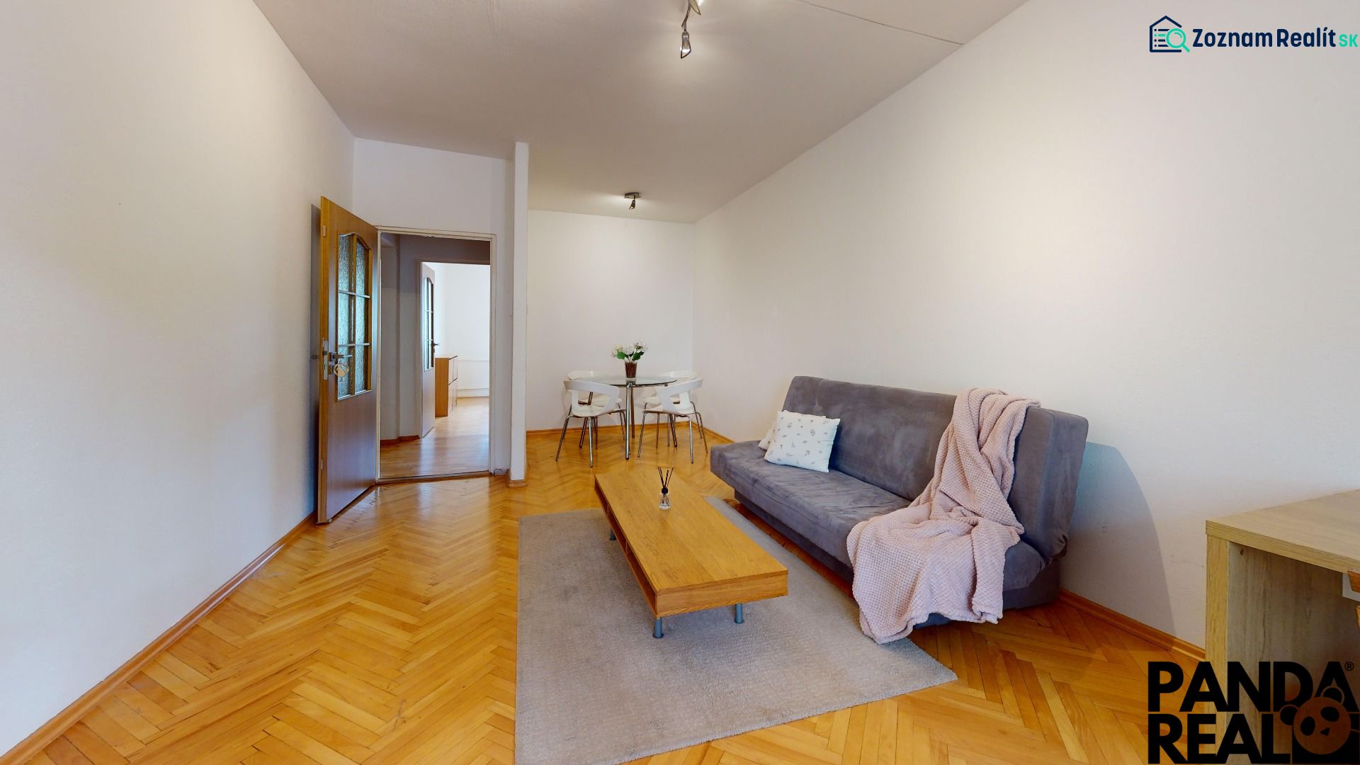 Living room in a two-room apartment with a wooden decor floor and simple furnishings.