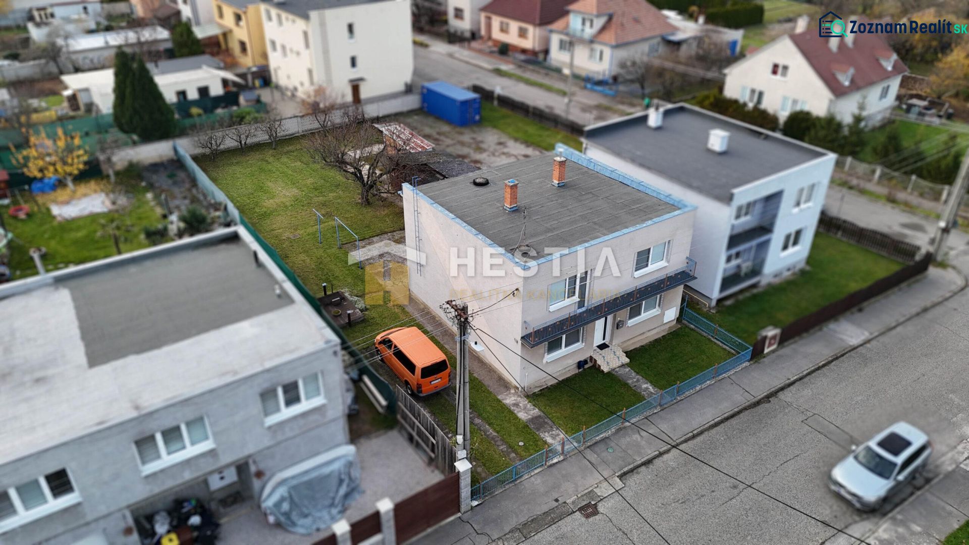 A family house in Senica with a fenced yard and a parked orange car.