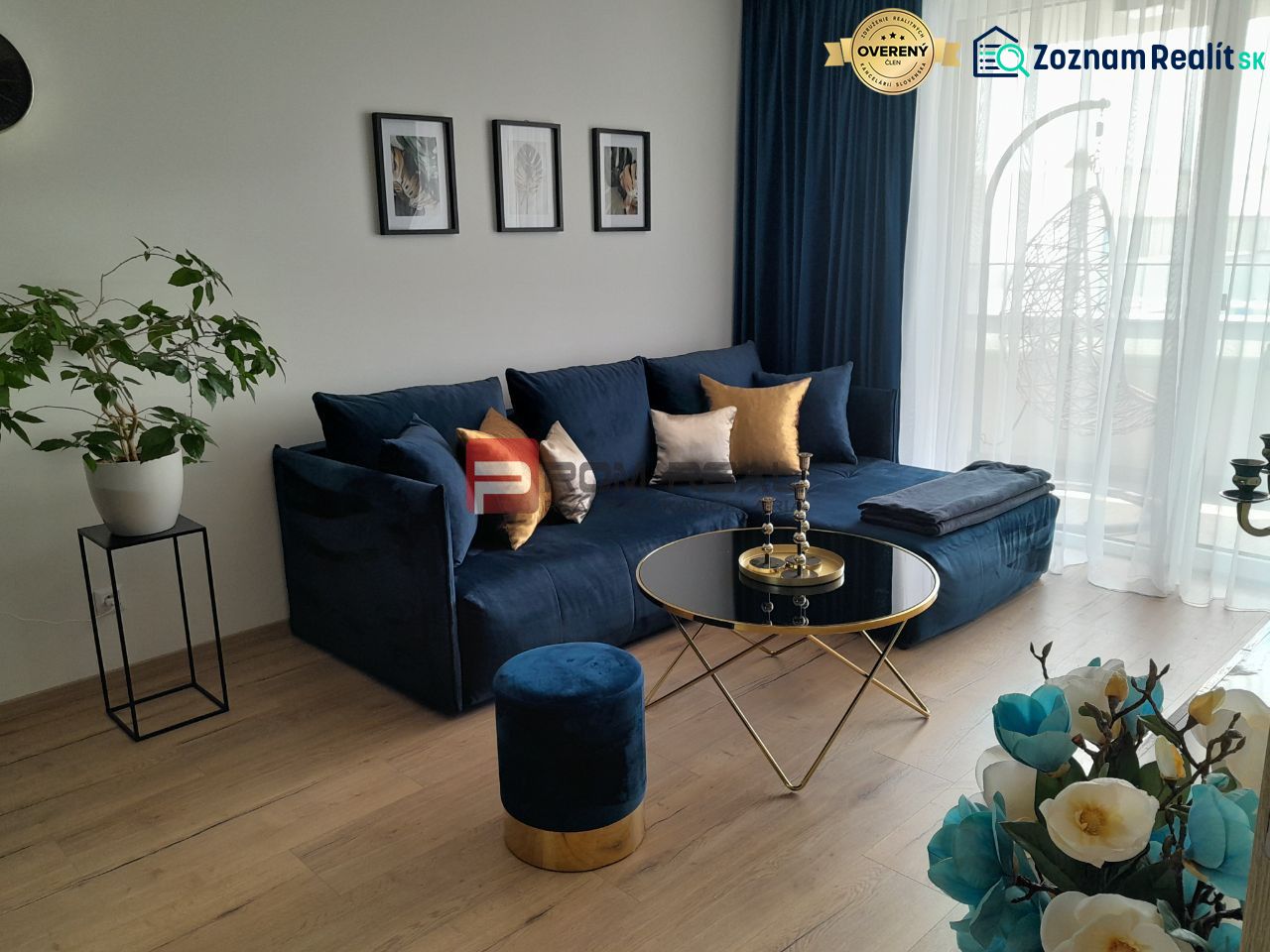 Living room in a two-room apartment with a blue sofa, wooden decor flooring, and decorations.