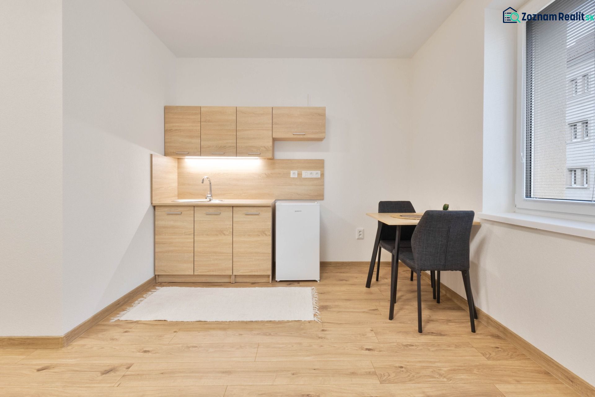 Studio apartment with a kitchenette, refrigerator, and table, complemented by a floor with a wooden decor.