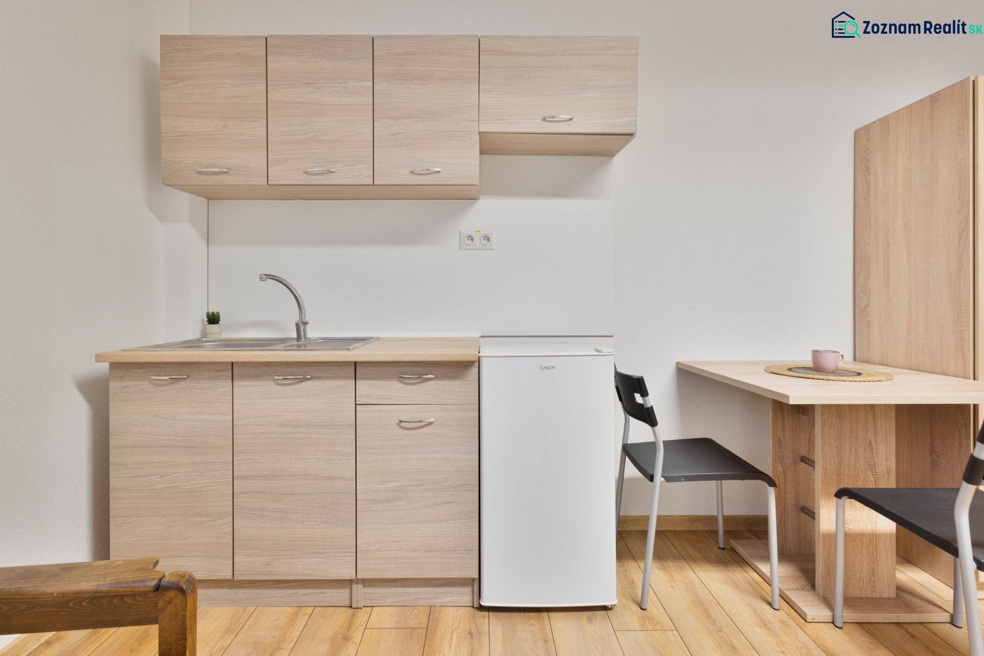 A kitchenette in a studio apartment with a white refrigerator and a wooden decor floor.