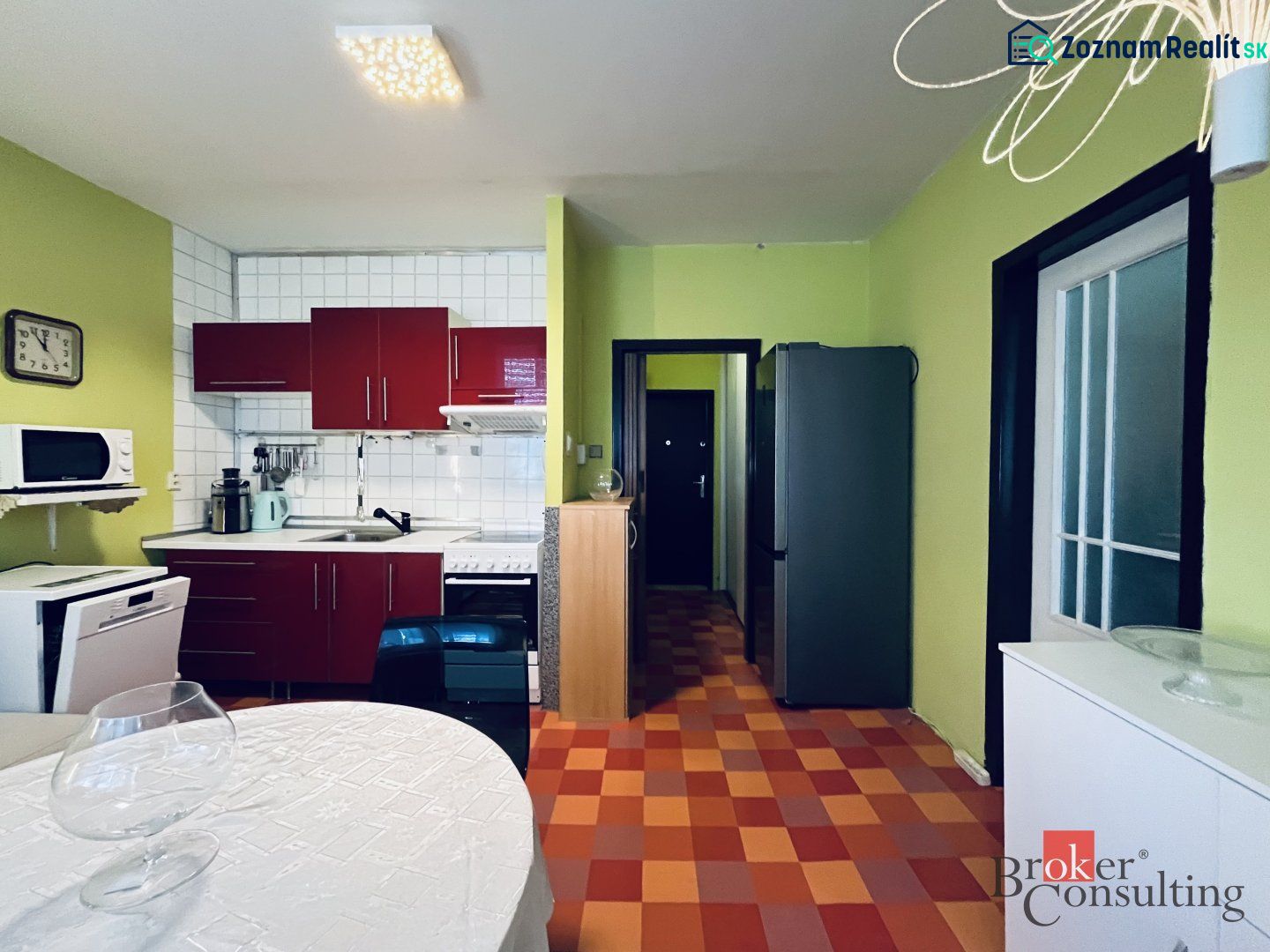 A kitchen in a studio apartment with colorful tiles, white tiles, and green walls.