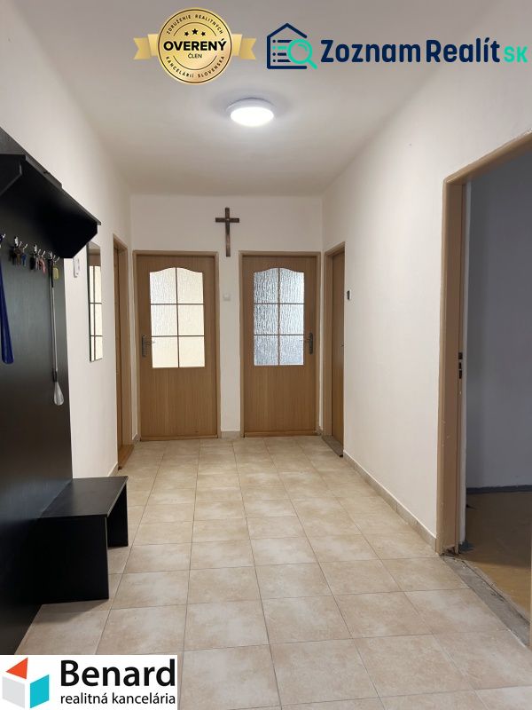 A hallway in a family house with tiles, wooden doors, and a coat rack.