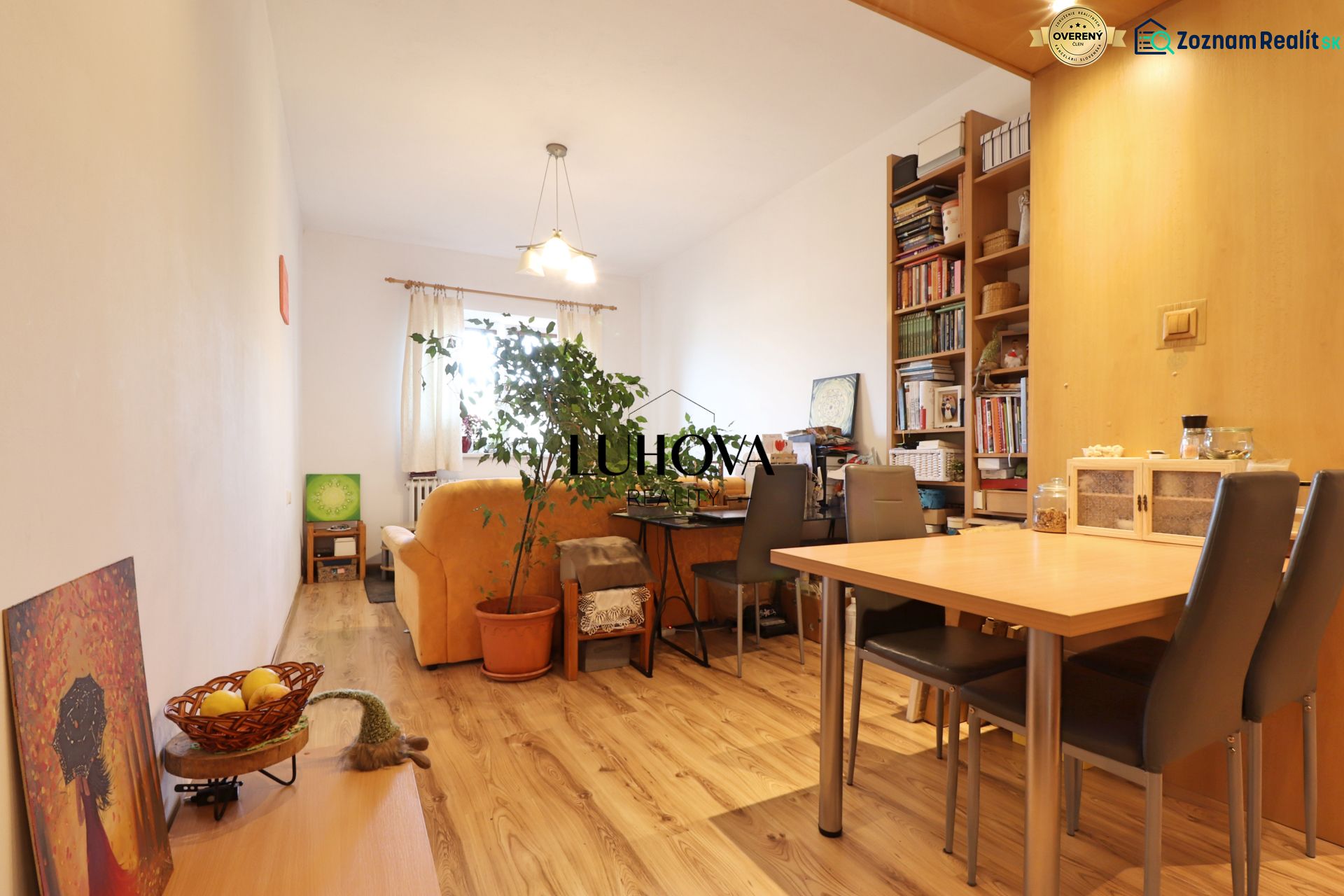 Living room with wood-patterned flooring, a sofa, a table, and a bookshelf in a two-room apartment.