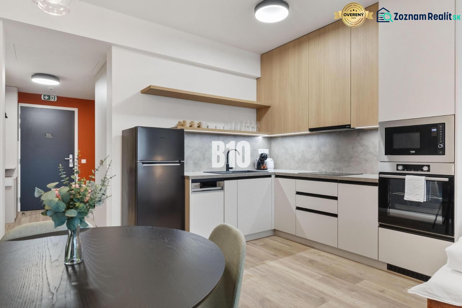 A kitchen with a dining table, appliances, and a wooden decor floor in a studio apartment.