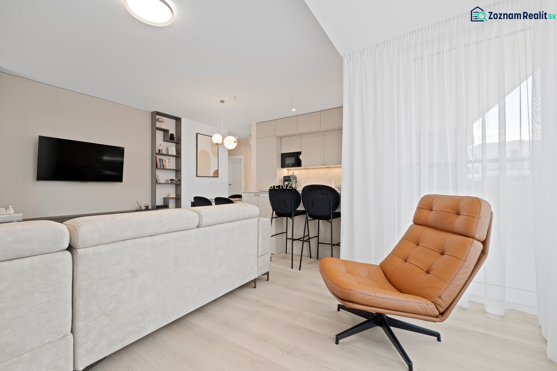 Living room in a three-room apartment with a wooden decor floor, a cream sofa, and a leather armchair.