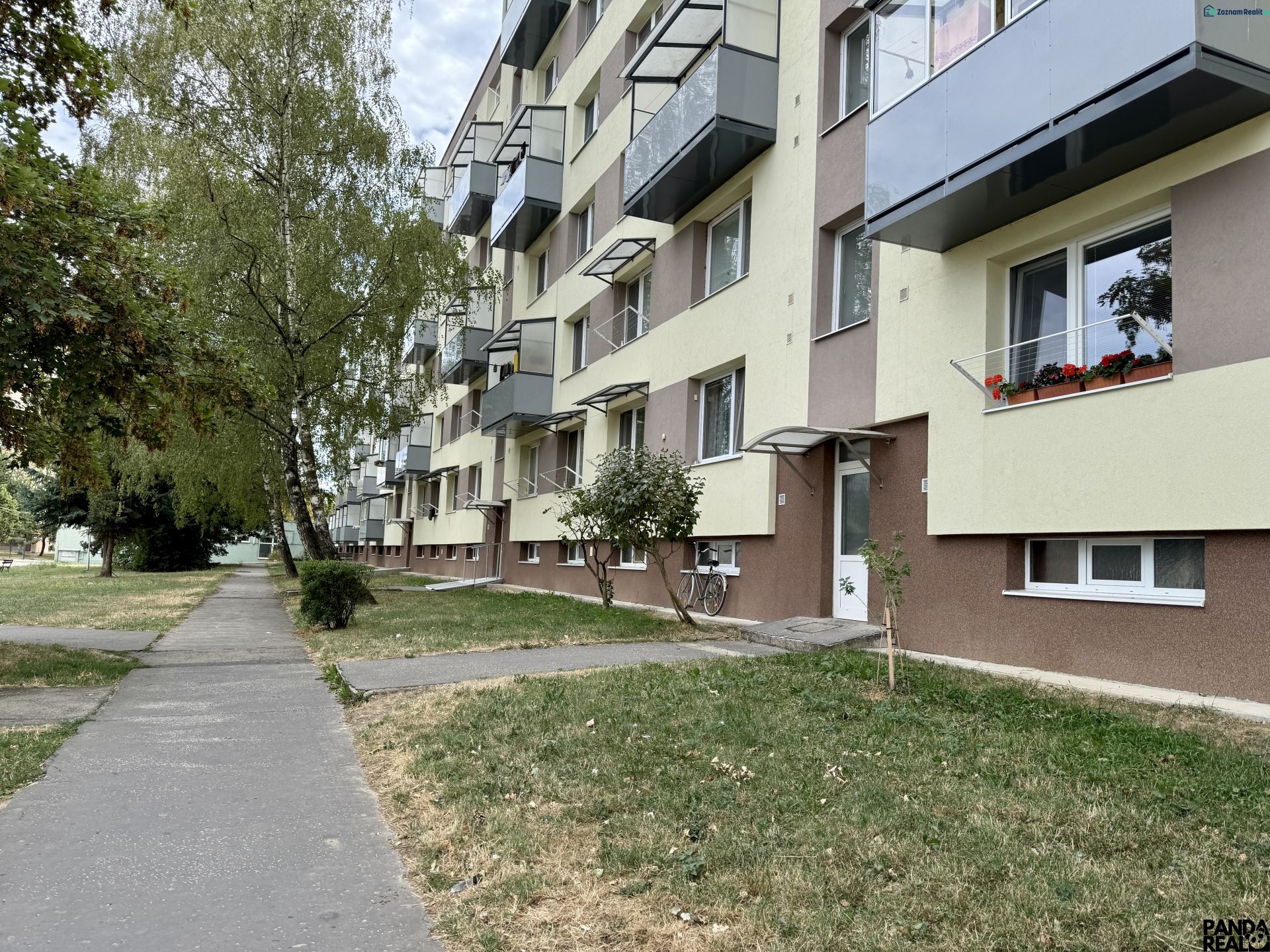 An apartment building with greenery and a walkway, located in Topoľčany, surrounded by trees.