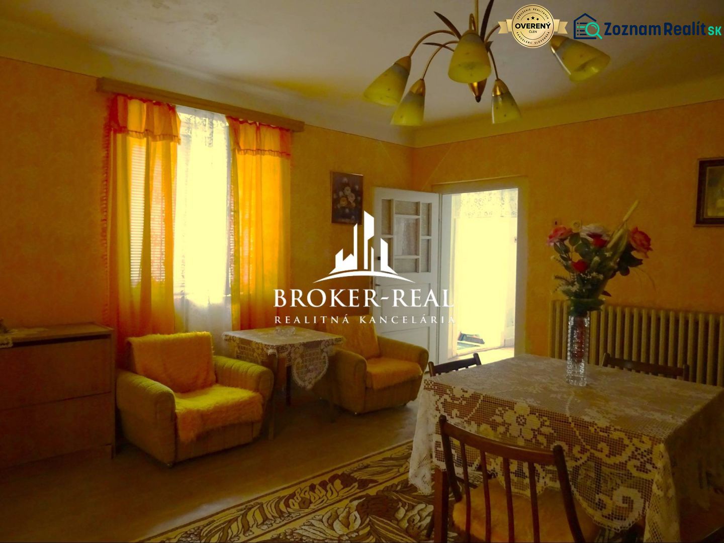 A living room in a family house with orange curtains and a table with a tablecloth.