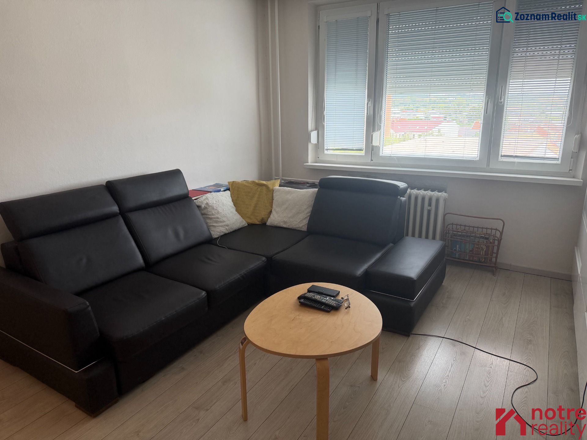 Living room in a two-room apartment with a black couch and a floor with a wood decor.