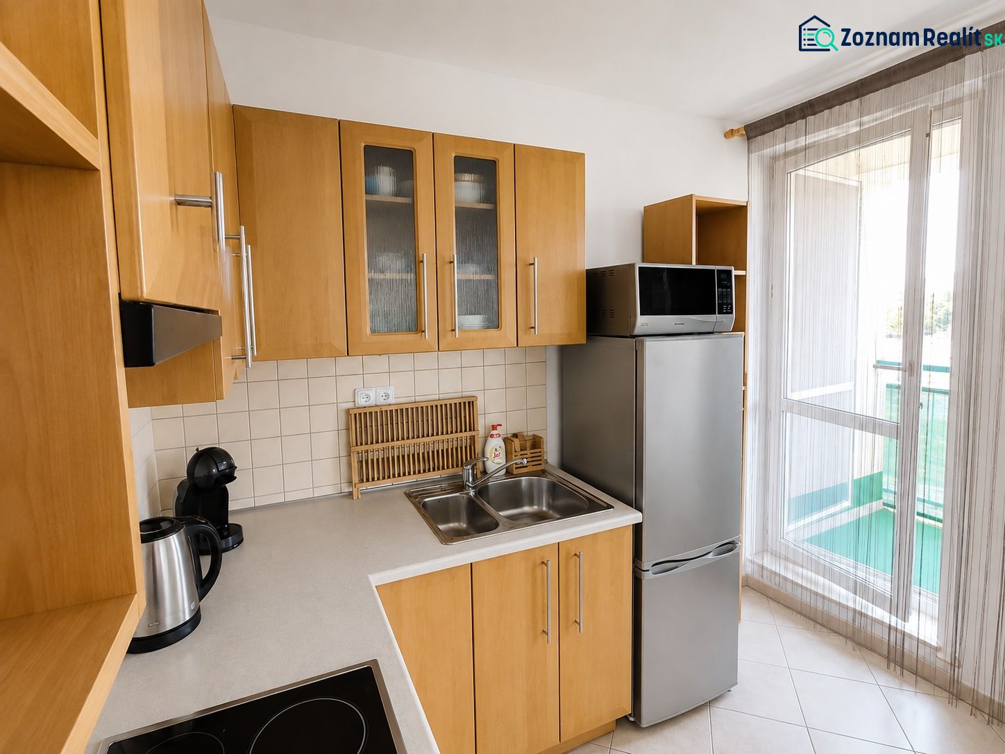 A kitchen with wooden cabinets, a refrigerator, and a microwave in a two-room apartment.