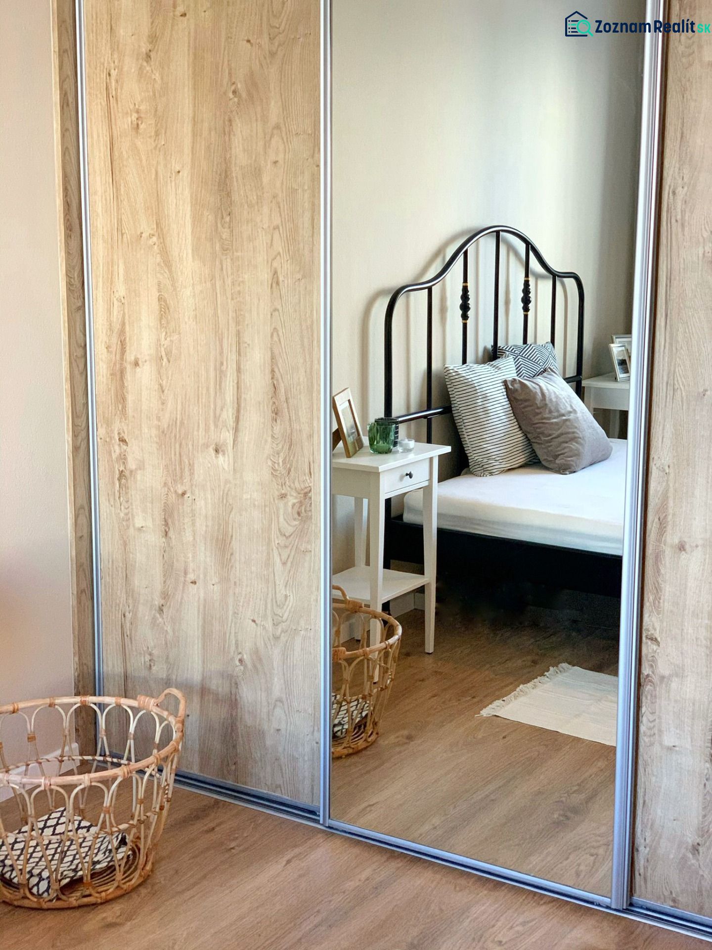 A mirrored wardrobe in a 2-room apartment with a wooden decor floor and a black bed.