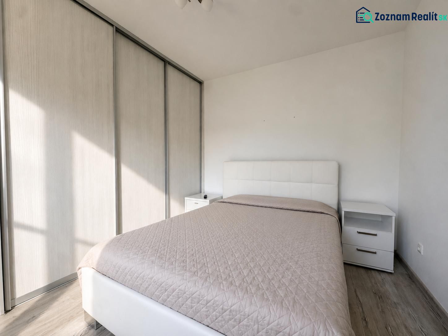 Bedroom in a two-room apartment with a wooden decor floor, a large wardrobe, and a bed.