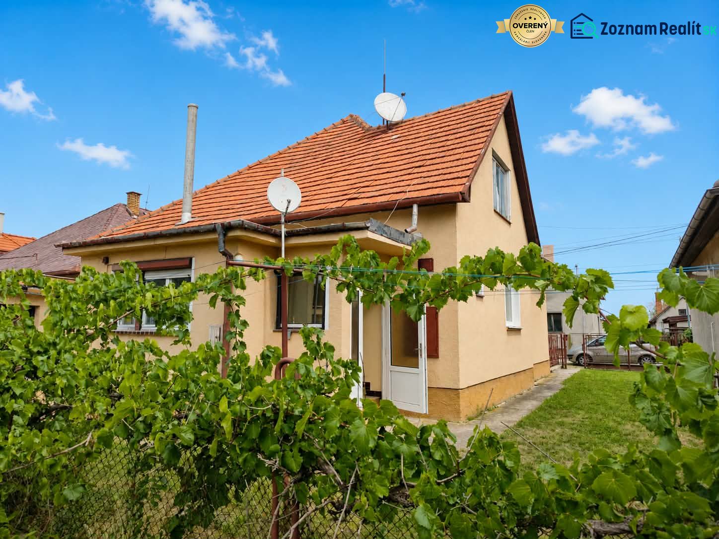 A family house in Oslany with a front garden, a fence, and a satellite dish on the roof.