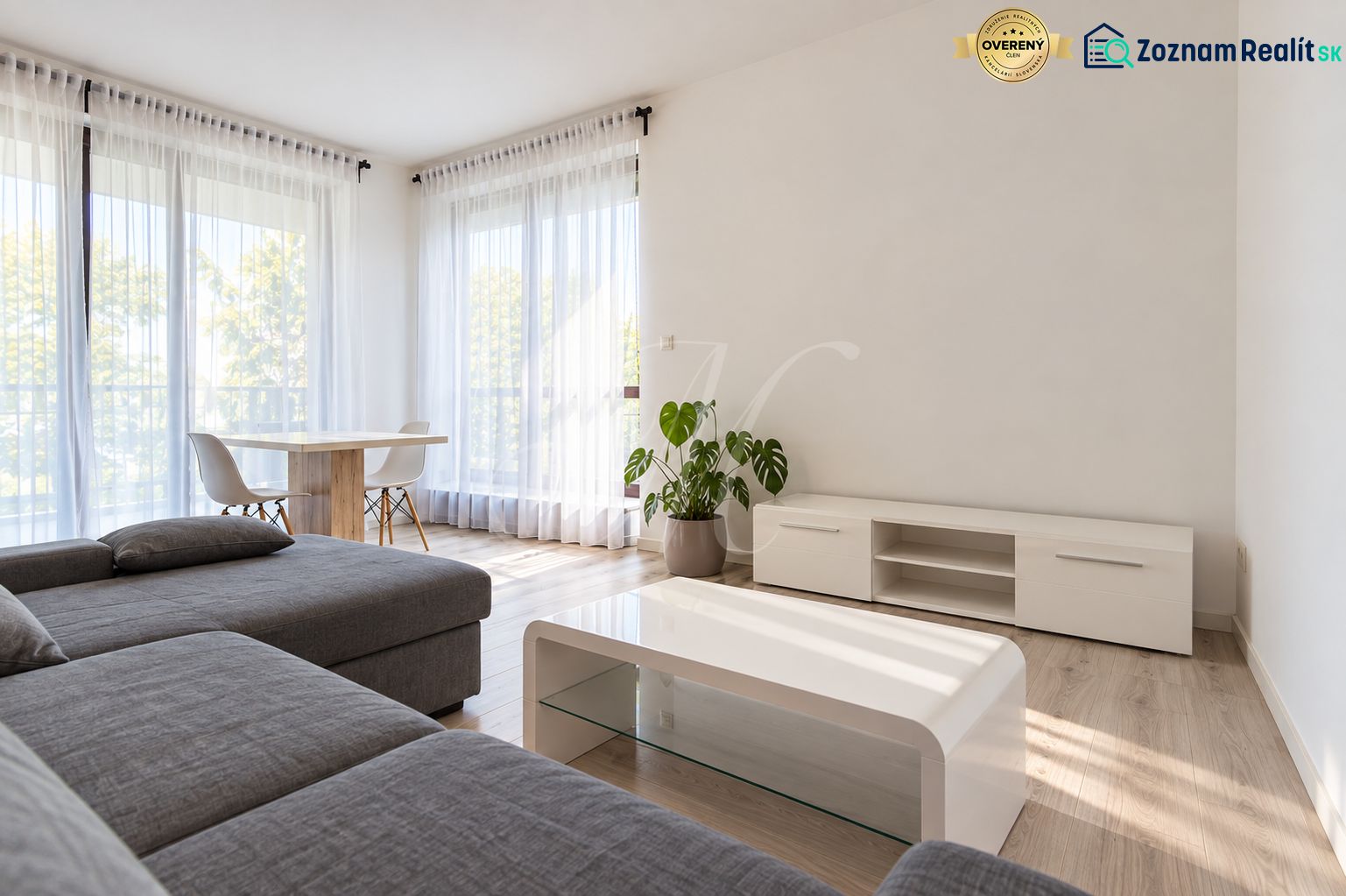 Living room of a two-room apartment with a wooden decor floor, a gray sofa, and a table.