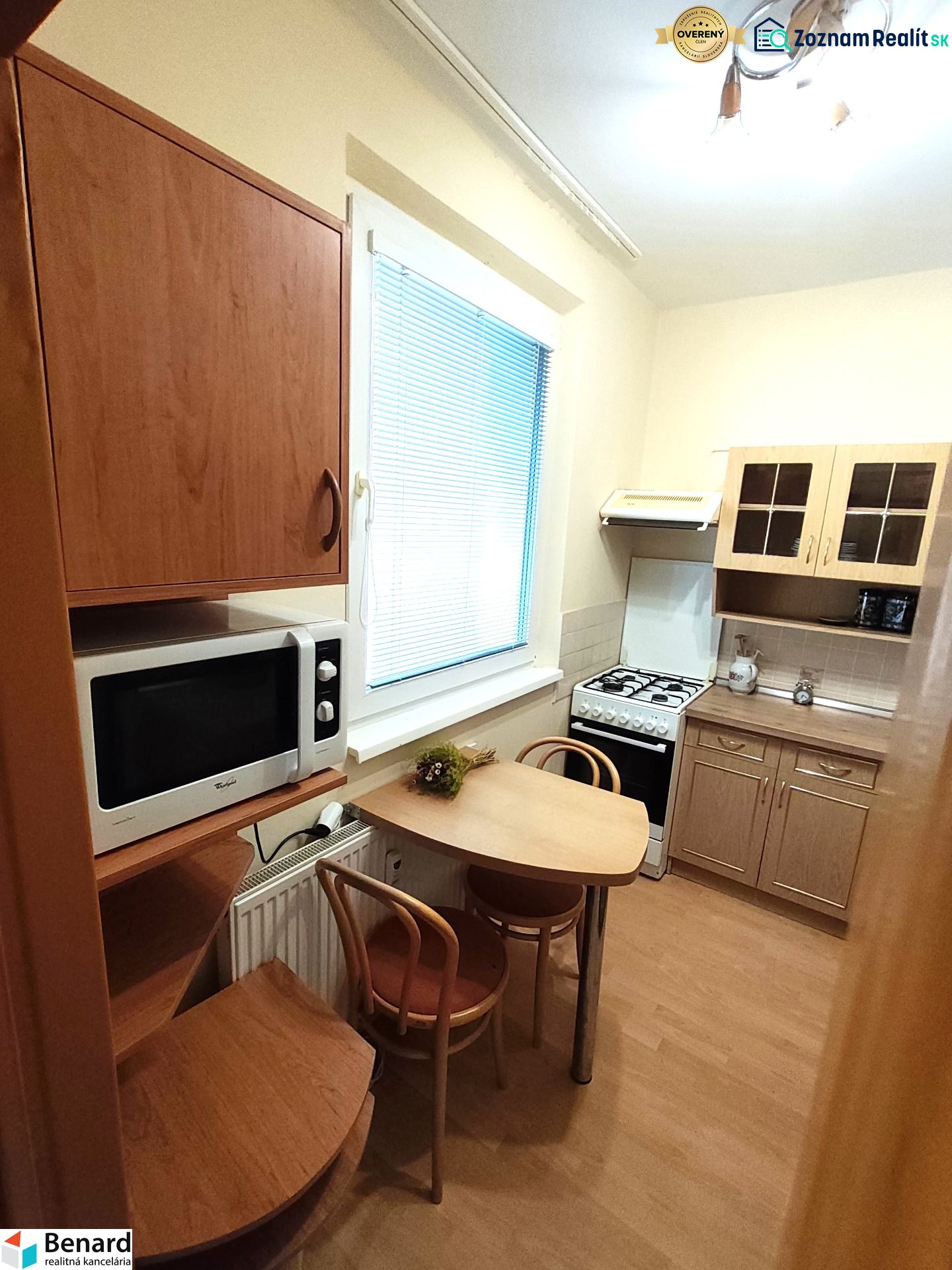 A kitchen in a studio apartment with a wooden decor floor, includes a table, microwave, and stove.