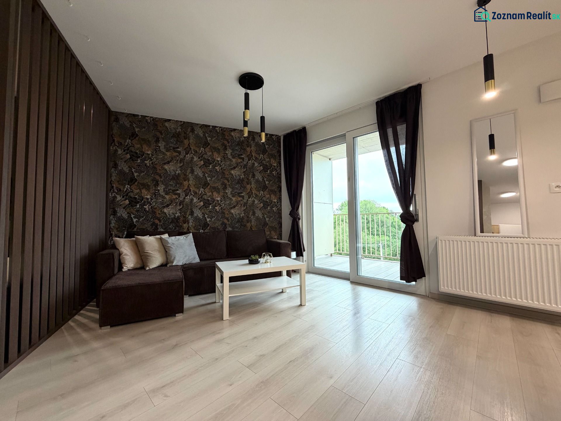 Living room in a two-room apartment with a sofa, balcony, and wooden decor flooring.