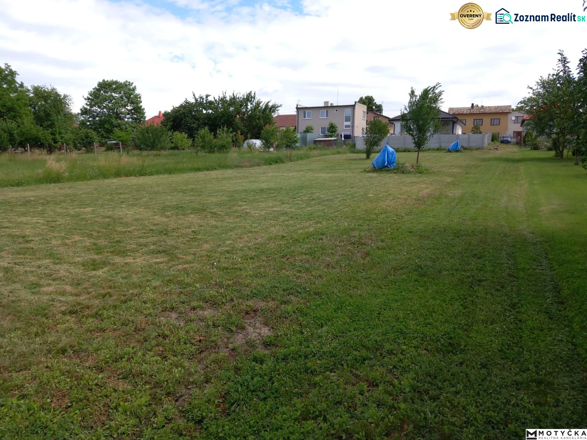 A garden with a lawn surrounded by houses in Beladice, designated for residential plots.