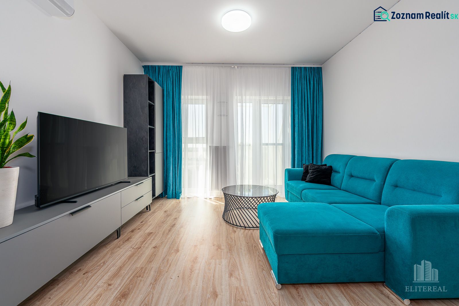 Living room in a two-room apartment with a wooden-patterned floor and a blue couch.