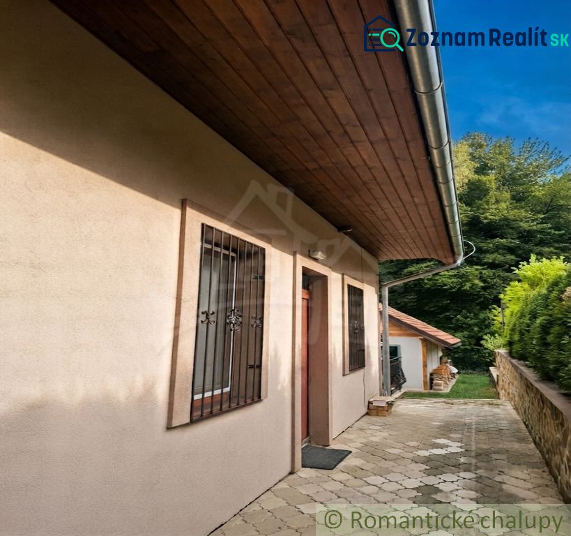 The exterior of the cottage in Ružiná with a paved walkway and wooden roof cladding.