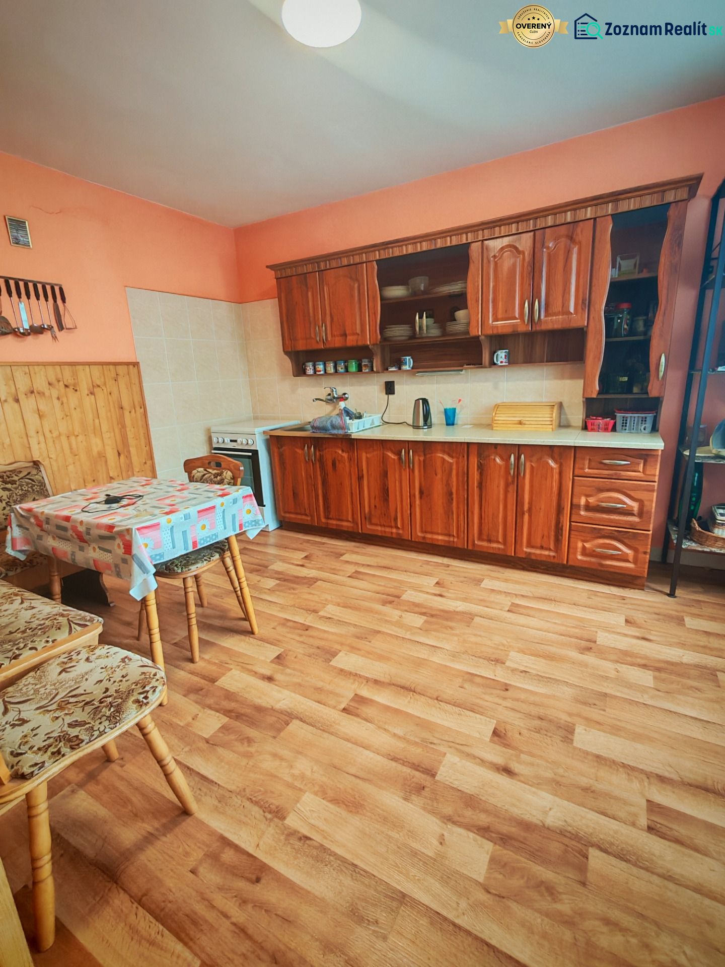 A kitchen in a family house with a wooden decor floor, a wooden kitchen unit, and a table with chairs.