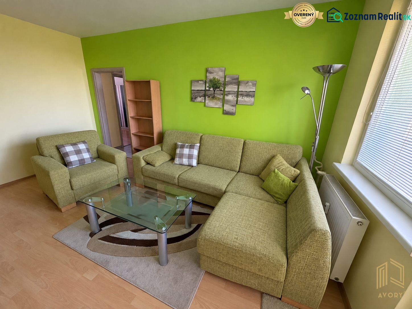 A living room in a two-room apartment with a green wall and a corner sofa.