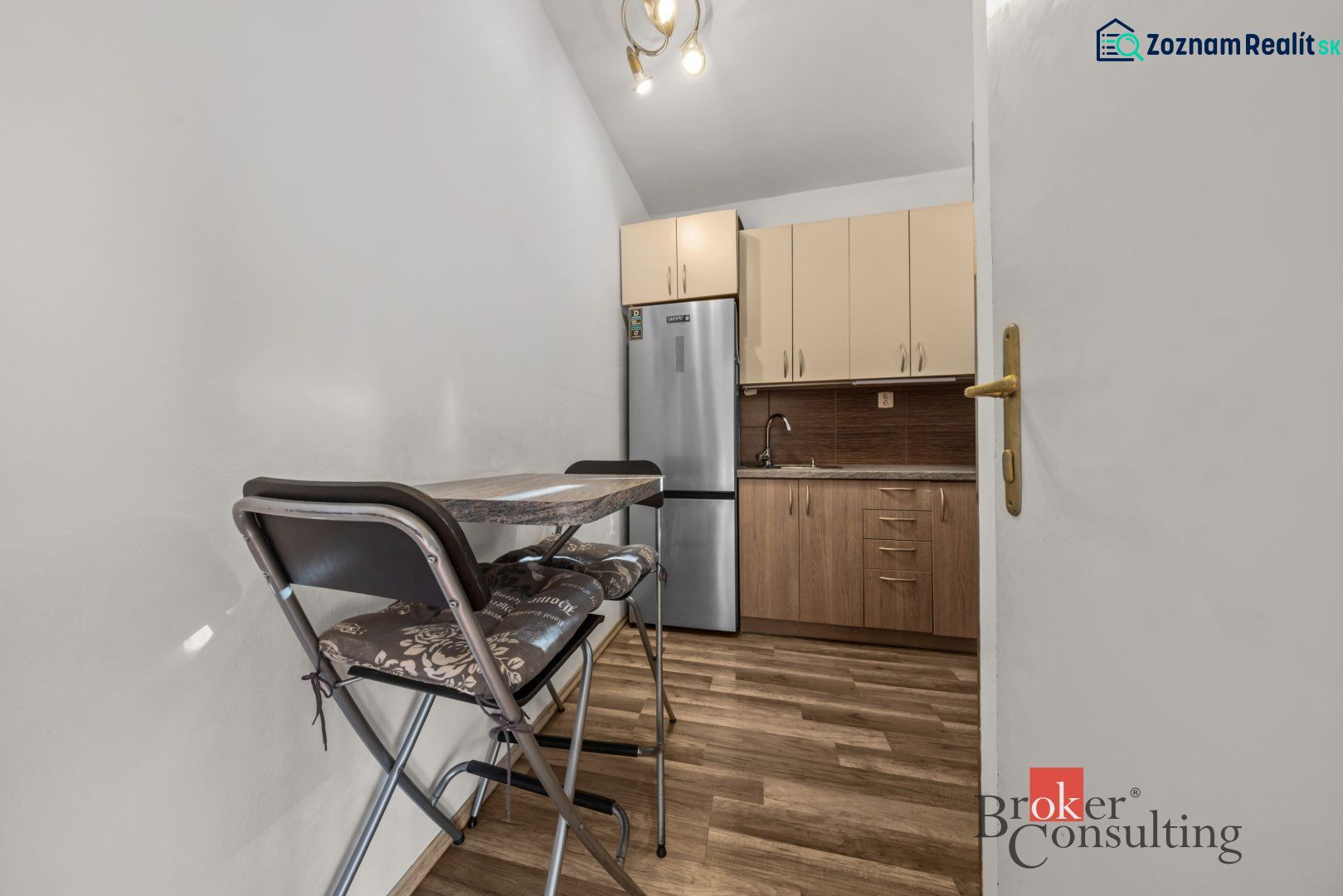 A kitchen in a 3-room apartment with a kitchen unit, appliances, and a floor with a wood decor.