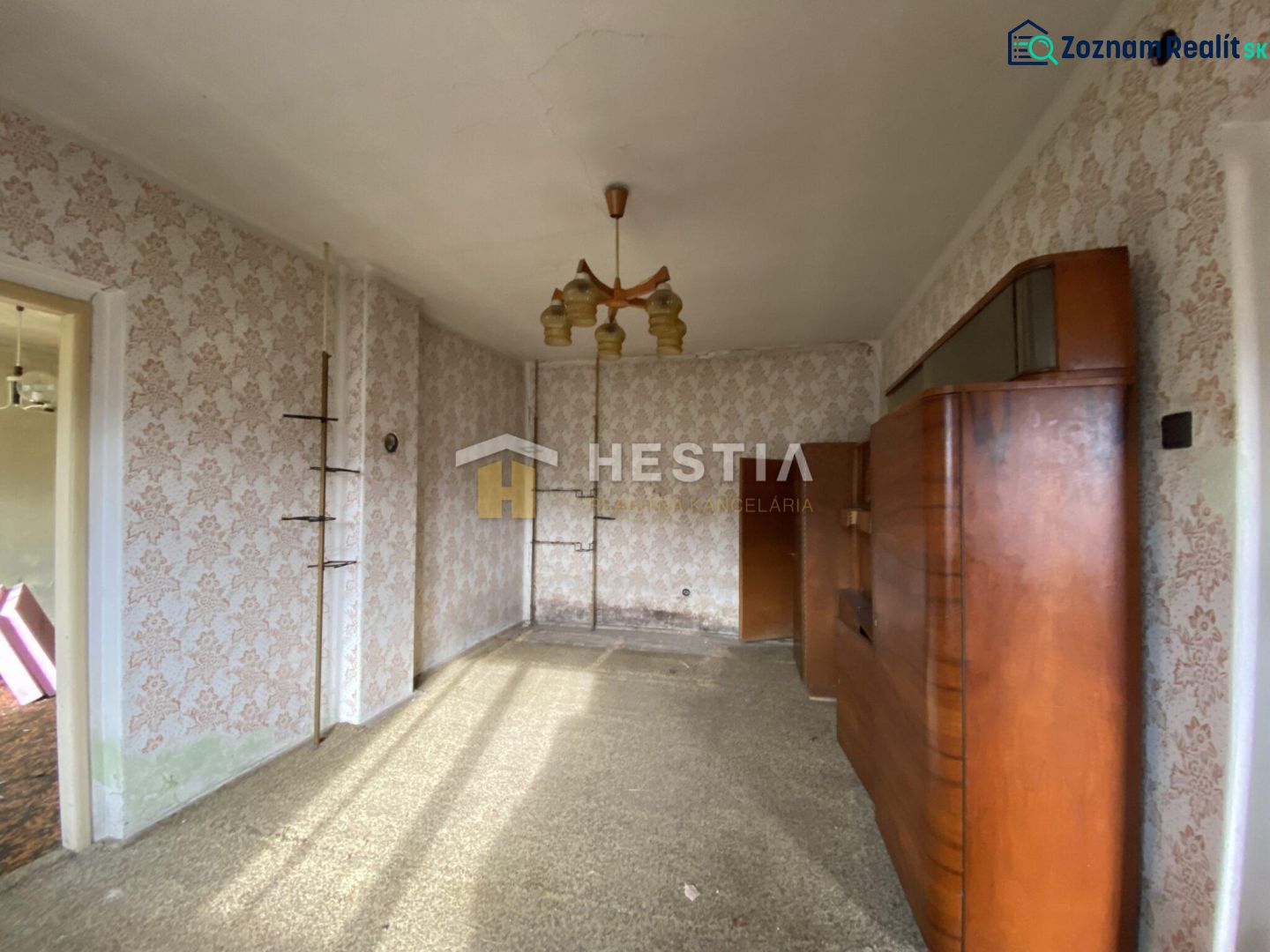 A room in a family house with wallpaper, older furniture, and a chandelier.