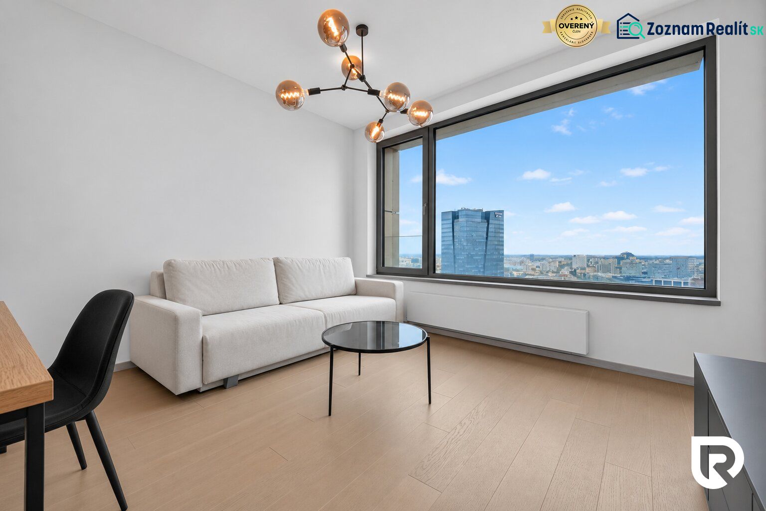 A room with a sofa, a table, a large window, and a wooden-patterned floor in a two-room apartment.