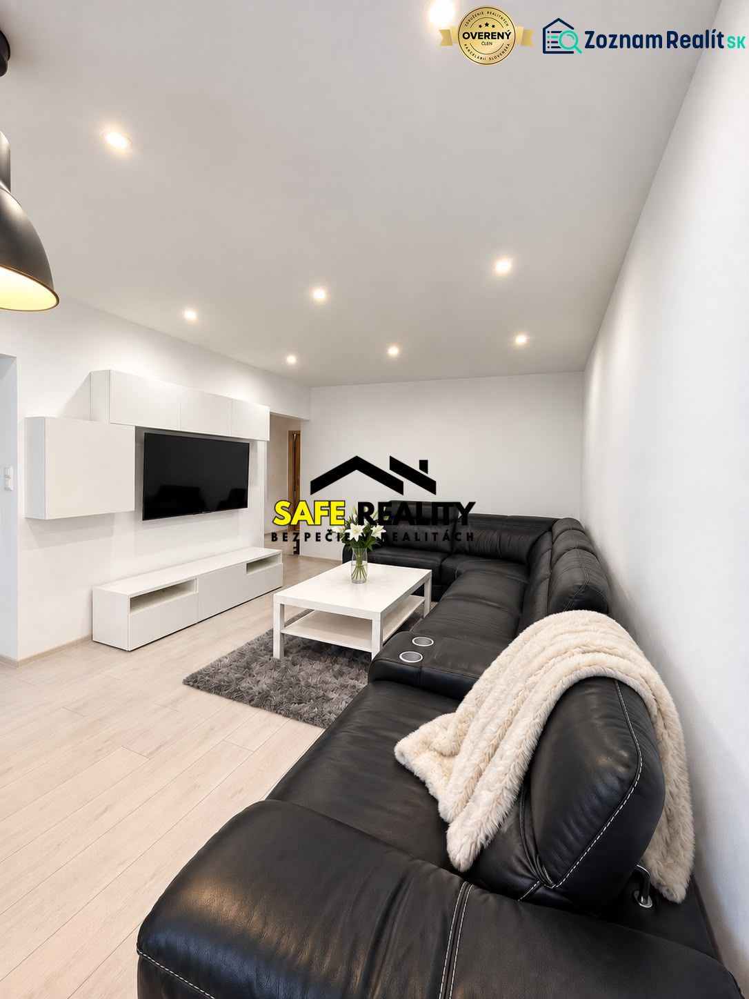 Living room in a 3-room apartment with a large black sofa and a wooden decor floor.