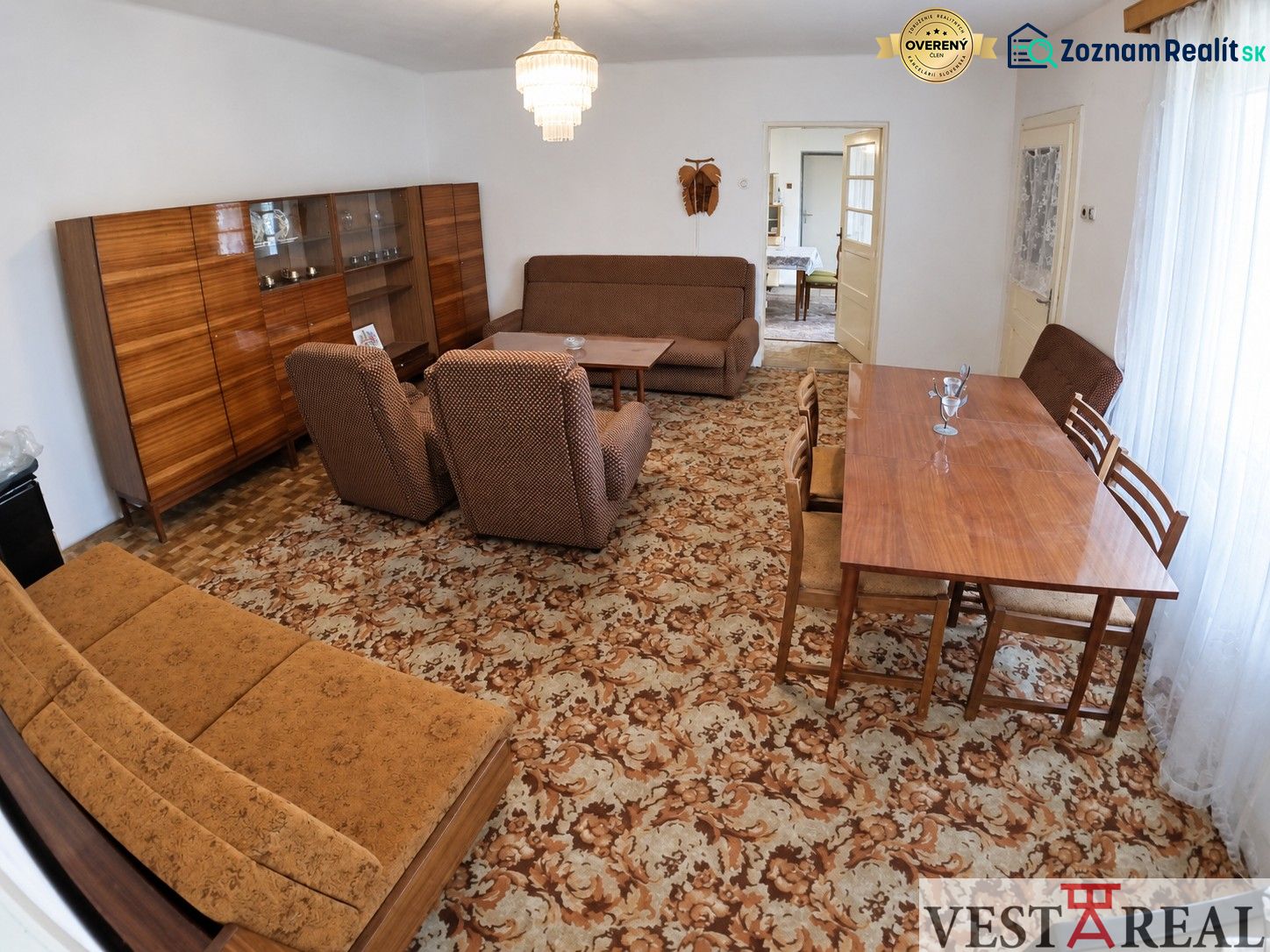 Living room in a family house with carpet pattern, wooden furniture, and a chandelier.