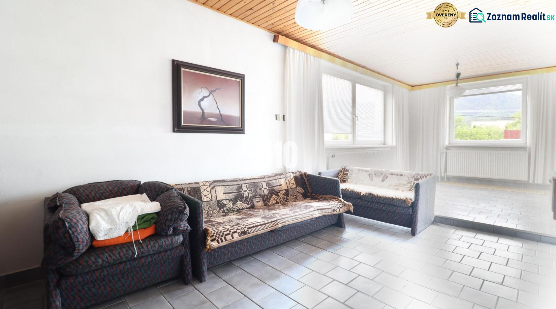 A room in a family house with a sofa, a painting on the wall, and large windows.