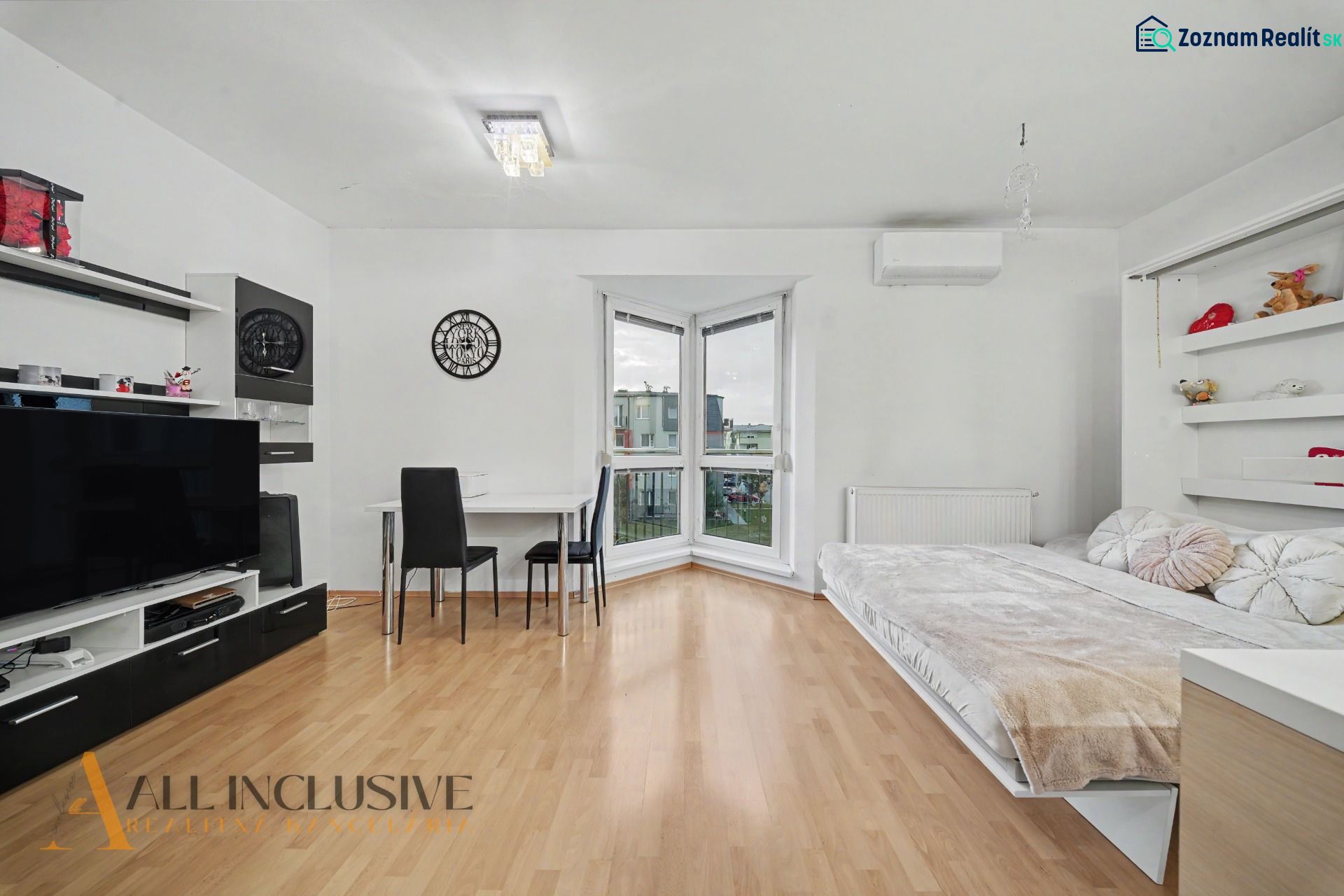 Living room with wood-patterned flooring, a bed, and a table in a studio apartment.