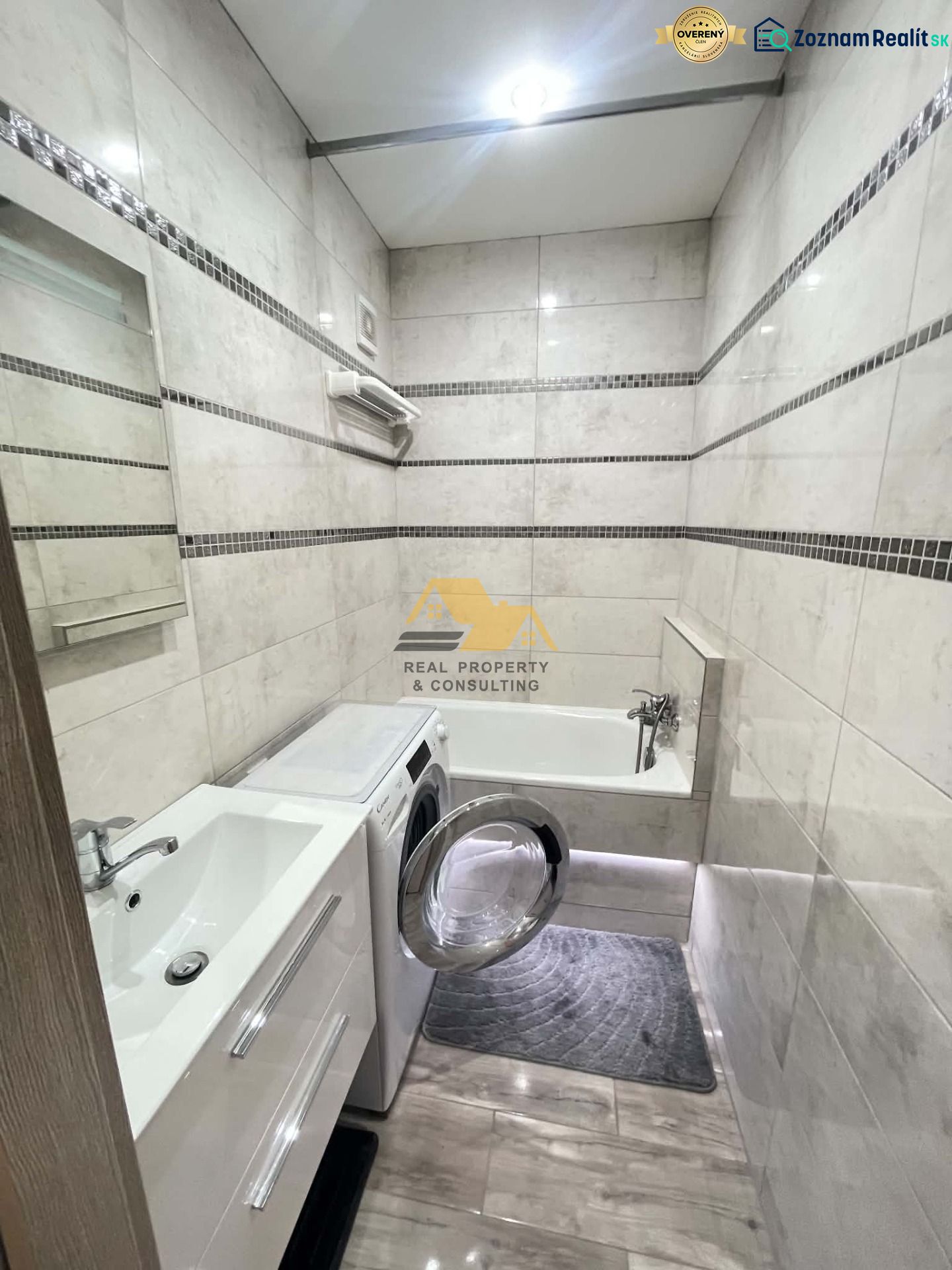 A bathroom in a studio apartment with a shower, a washing machine, and a wooden-patterned floor.