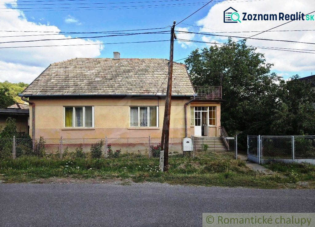 A family house in Sečianky with a garden, fence, and veranda on a sunny street.