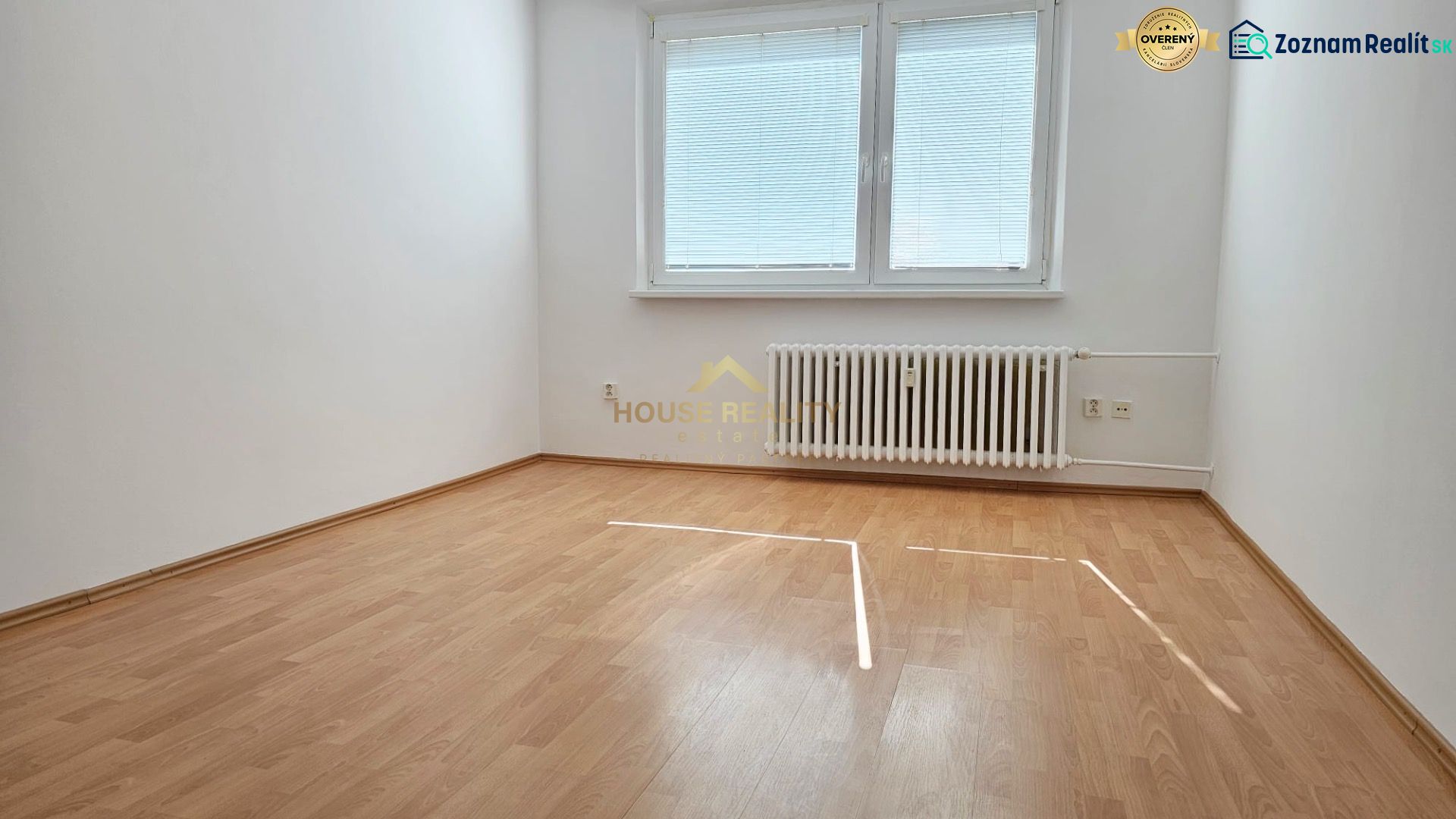 Empty room with wood-patterned flooring, radiator, and window with blinds.
