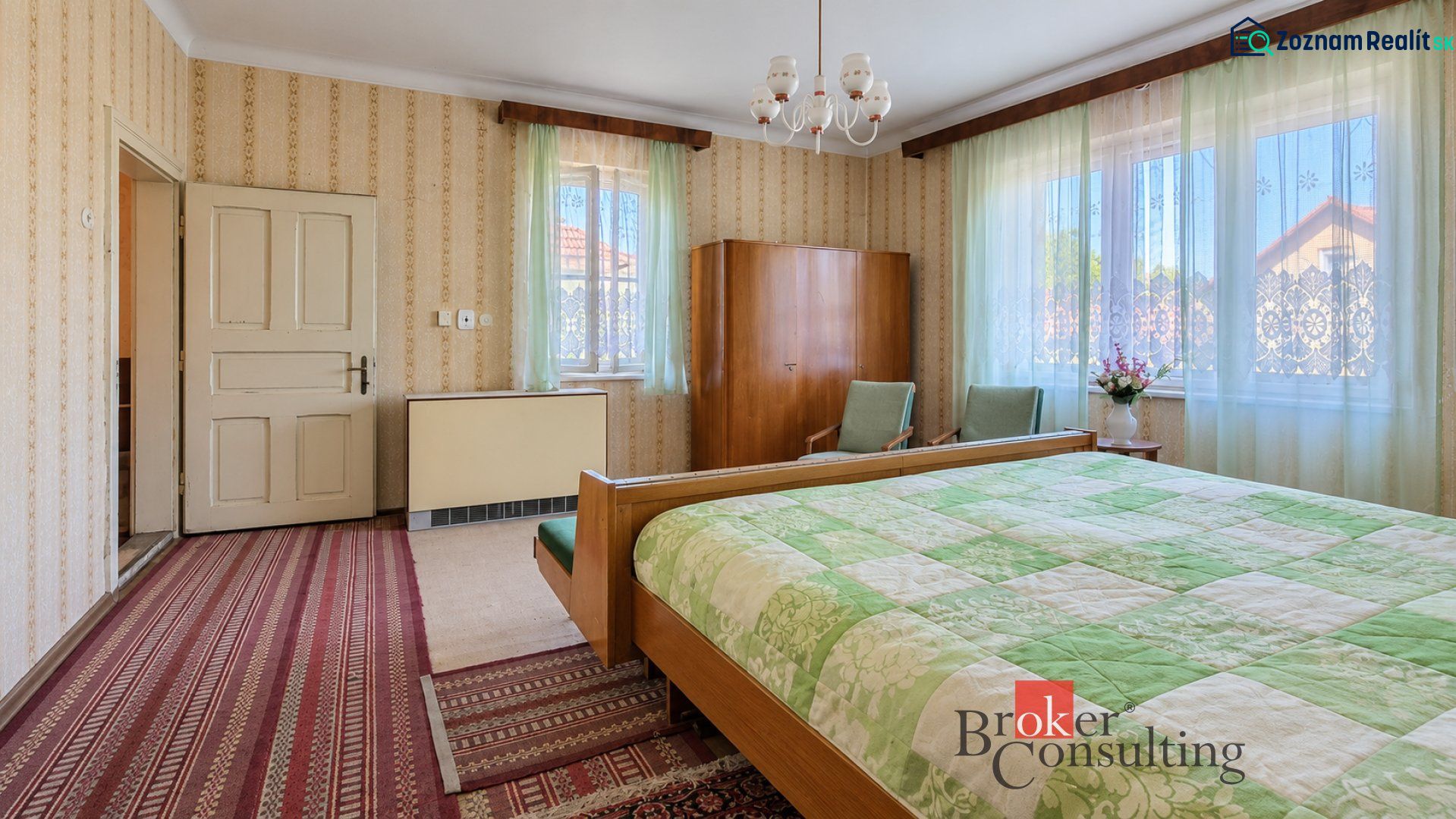 A bedroom in a family house with vintage furniture, wallpaper, and green curtains.