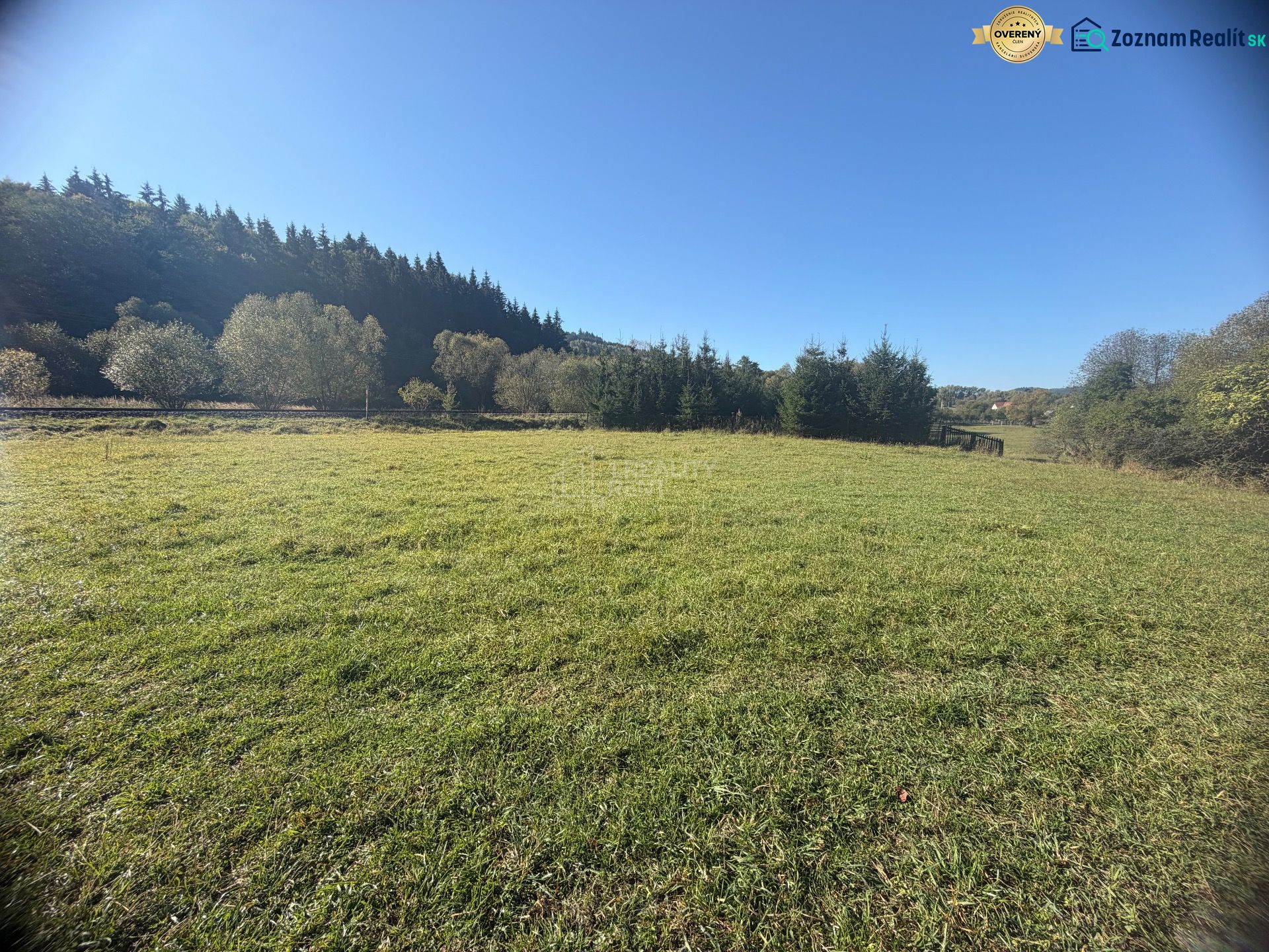Plots - housing in Podvysoká, flat grassy area surrounded by trees with a clear sky.