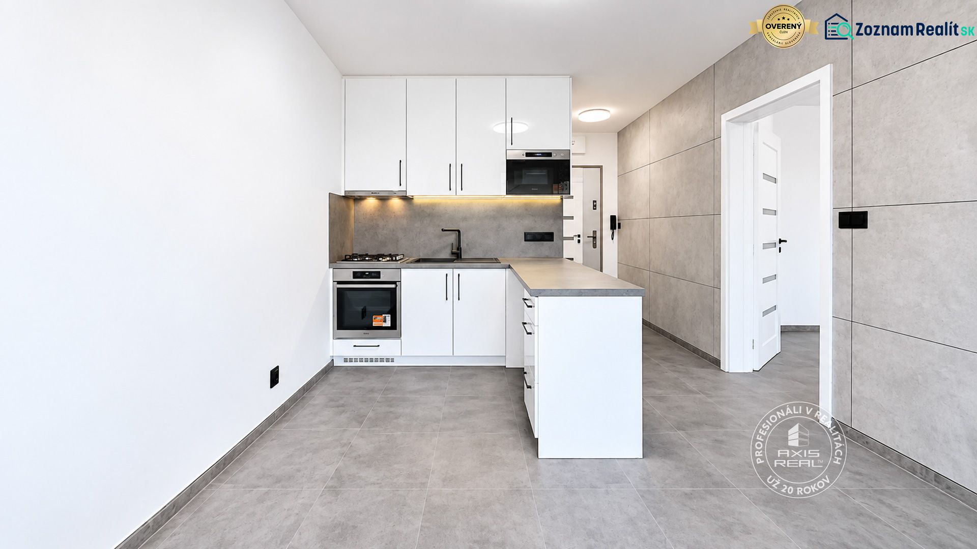 A kitchen in a 2-room apartment with white cabinets and gray tiles.