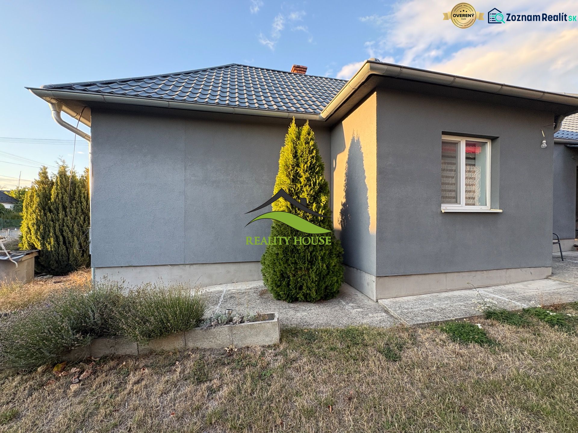 A family house in Blatné Revištia with a landscaped garden, gray facade, and hipped roof.