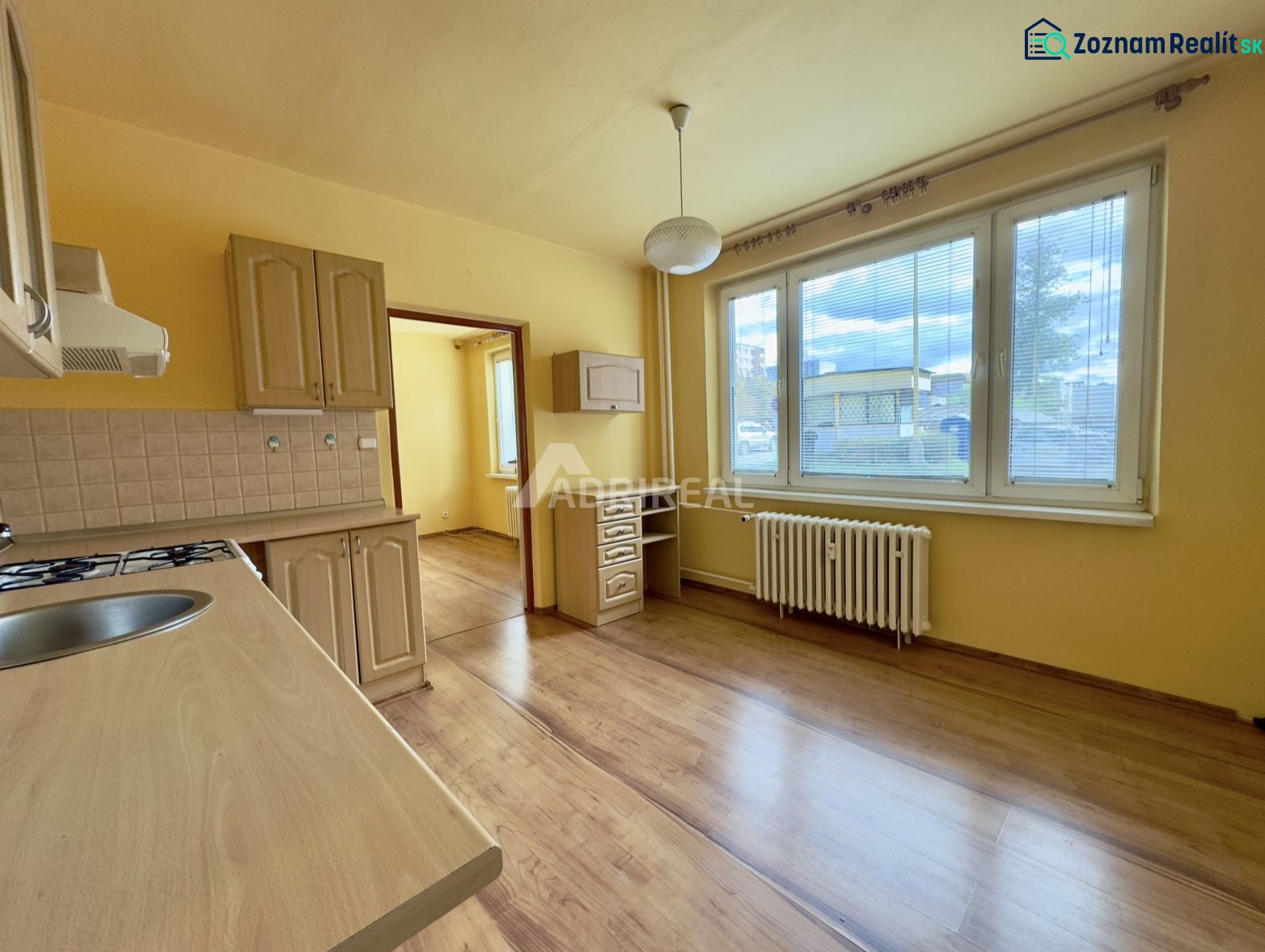 A kitchen with a wood-patterned floor, a countertop, and a large window in a studio apartment.