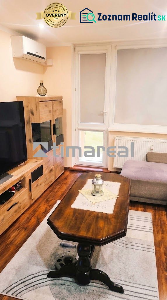 Living room in a 3-room apartment with a wooden decor floor, a sofa, and a television.