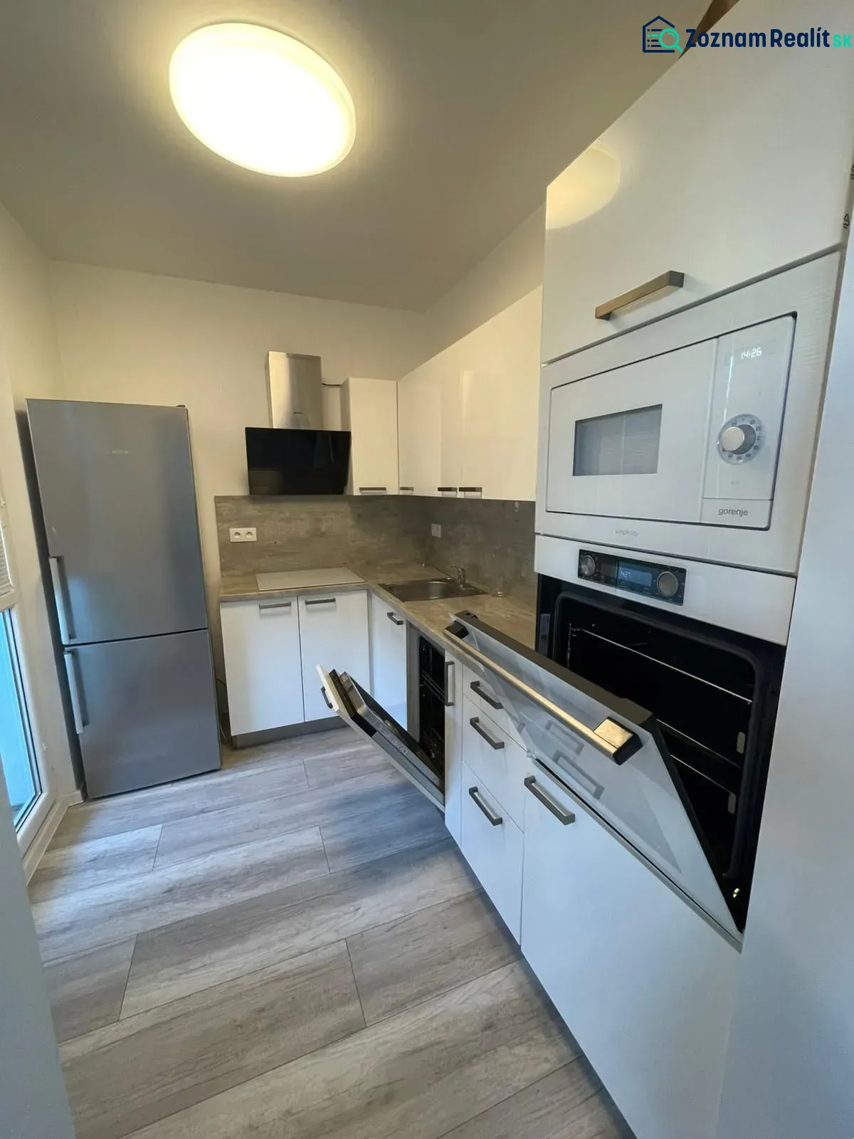 A kitchen with a built-in oven, white cabinets, and a wood-patterned floor in a 2-room apartment.