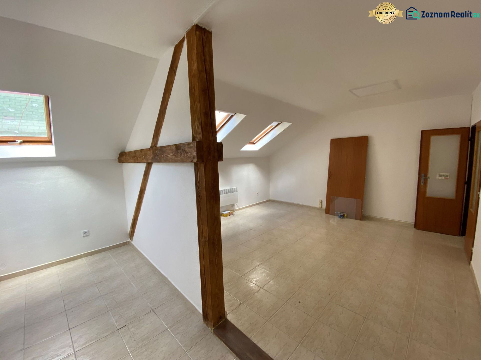 An attic office with wooden beams and slanted windows, floor with wooden decor.