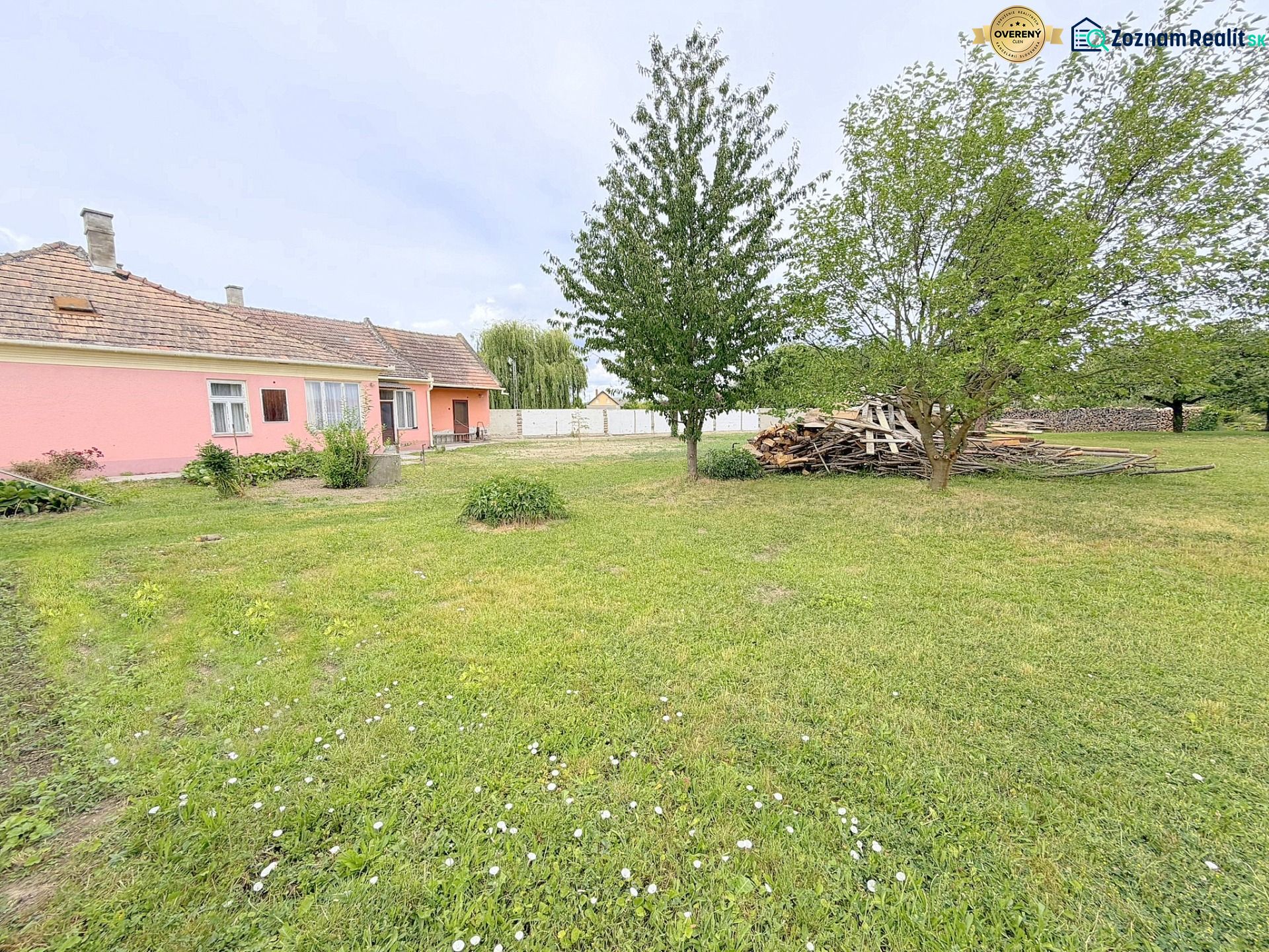 A family house in Dunakiliti with a pink facade surrounded by a spacious garden and trees.